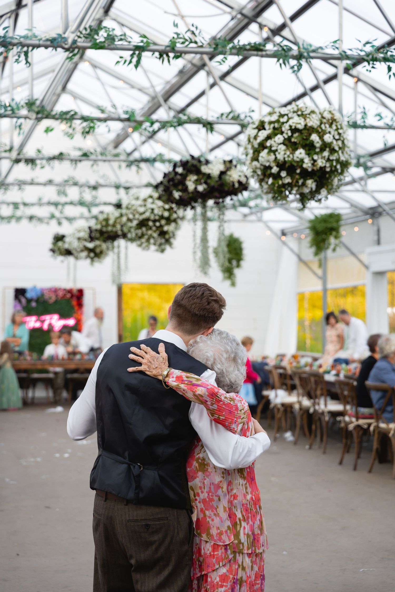 A series of four photos showing two people dancing together in a greenhouse venue with hanging floral decorations.