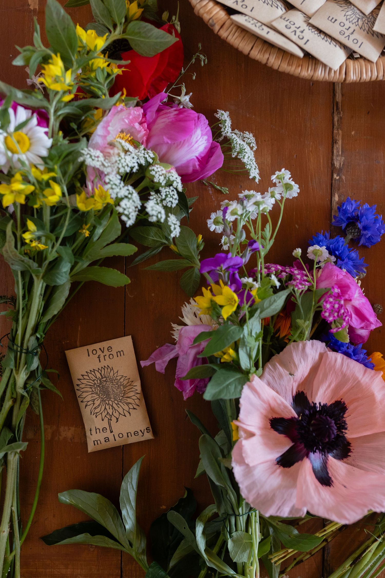 Fresh wildflower arrangement with pink poppies and seed packets on wooden table.
