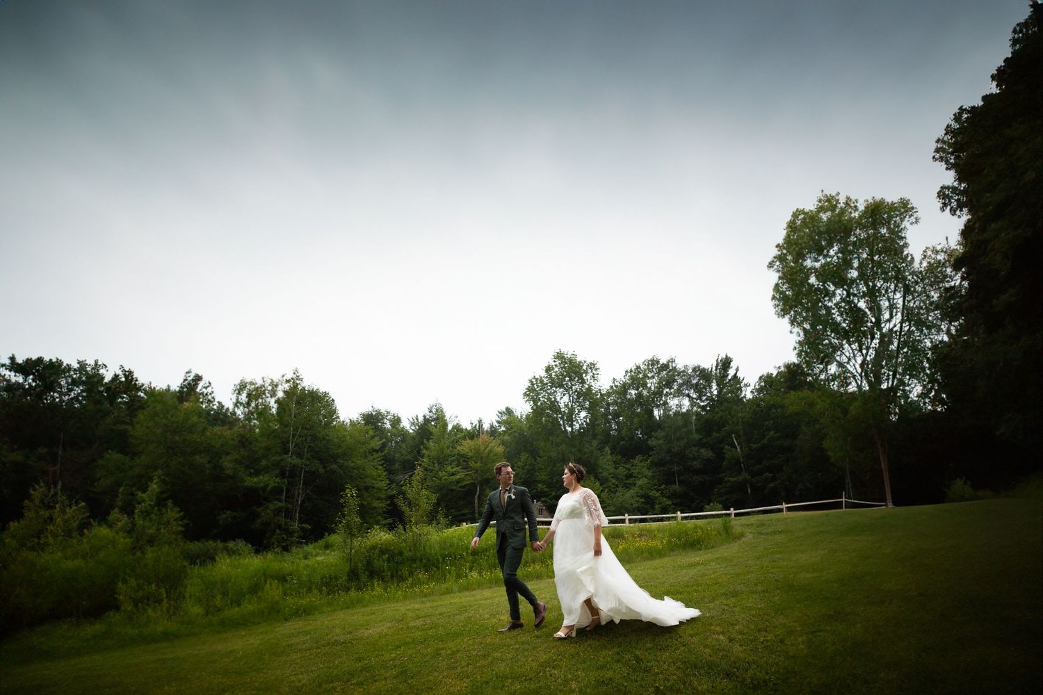 Artistic silhouette of wedding couple standing in field under moody sky.