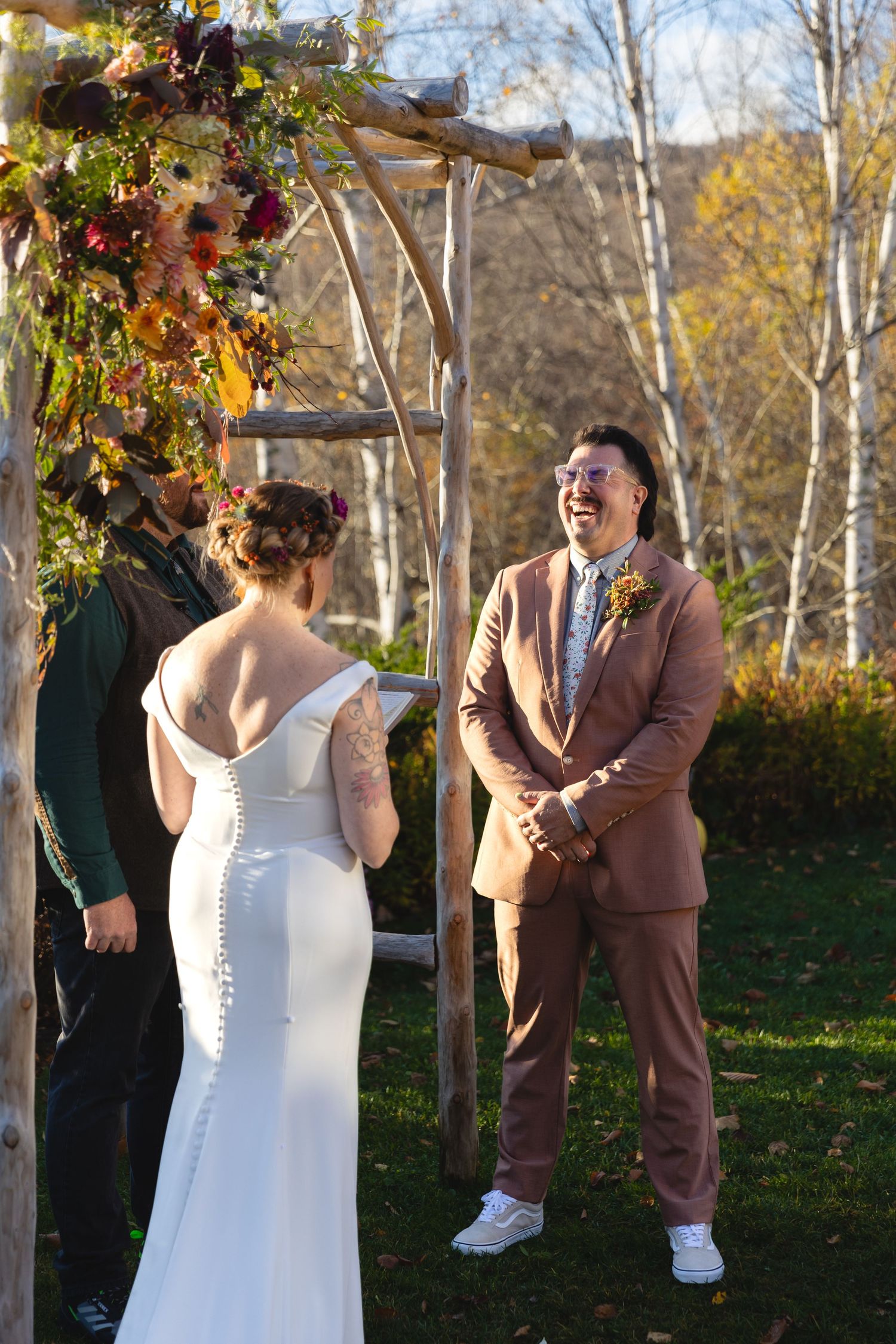 A joyful moment during an outdoor wedding ceremony beneath a floral-decorated wooden arch.