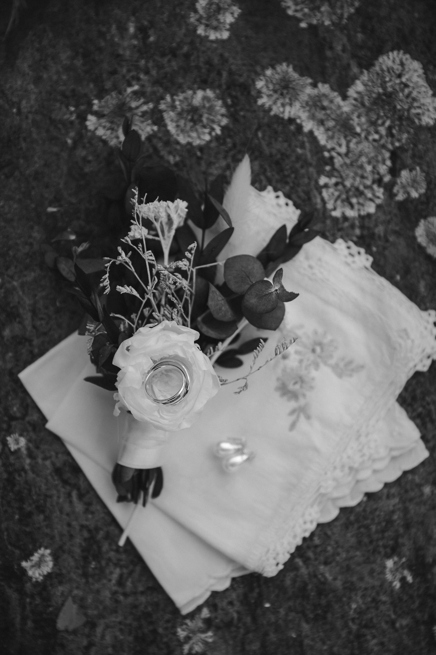 White rose bouquet and wedding ring arranged on lace fabric in monochrome.