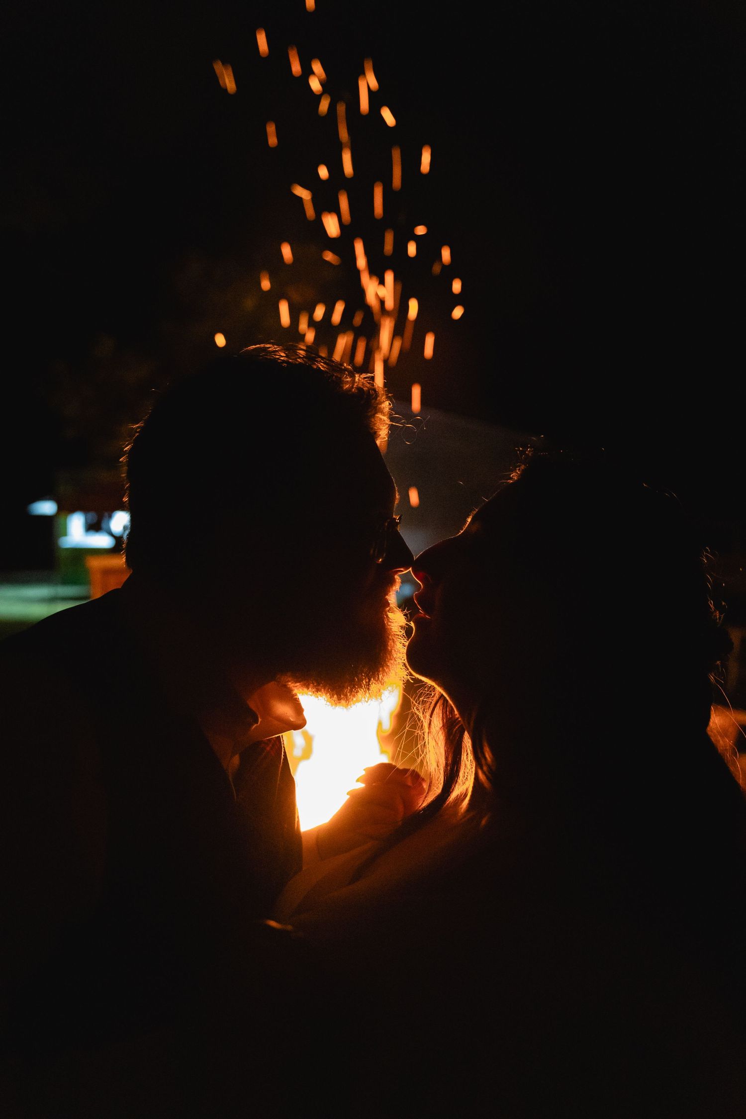 Silhouette with orange sparks flying against dark night sky near firelight.