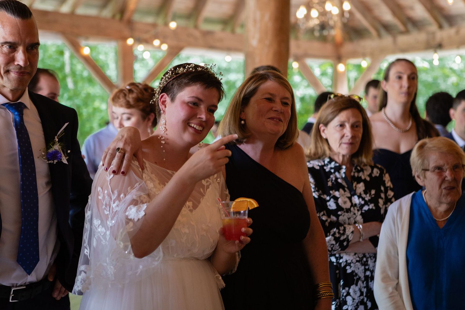 Wedding celebration with guests enjoying drinks and laughter at a covered outdoor venue.