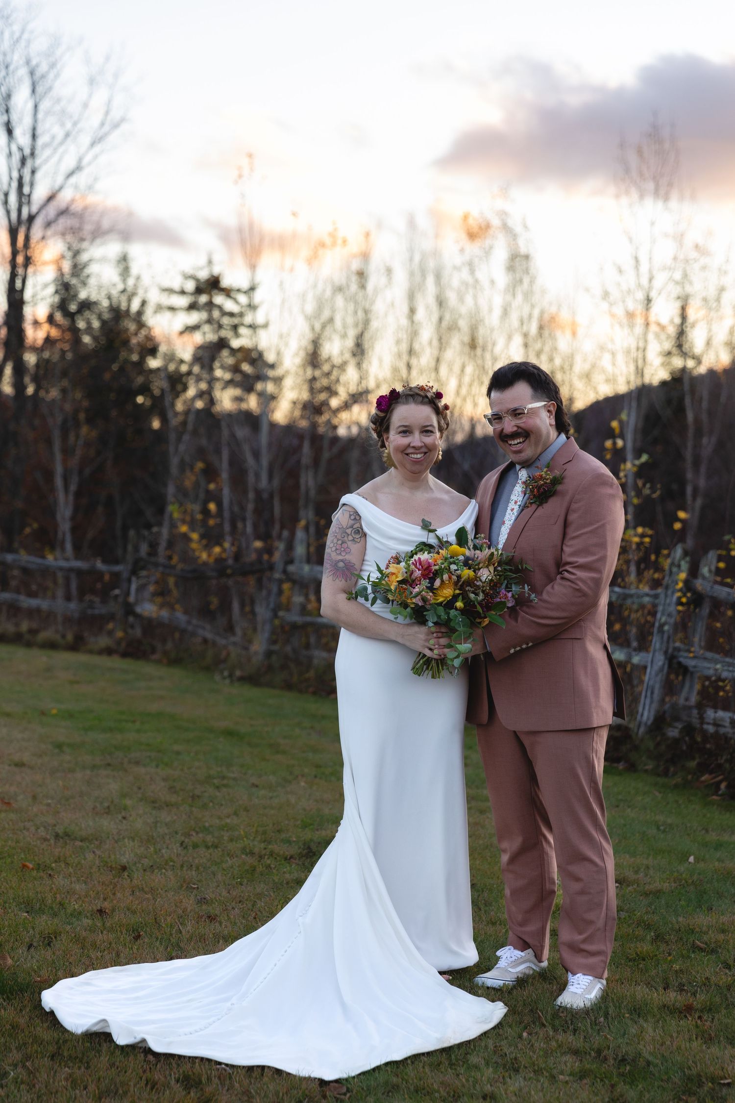Newlyweds pose together at sunset with a colorful bouquet and dusty pink suit.