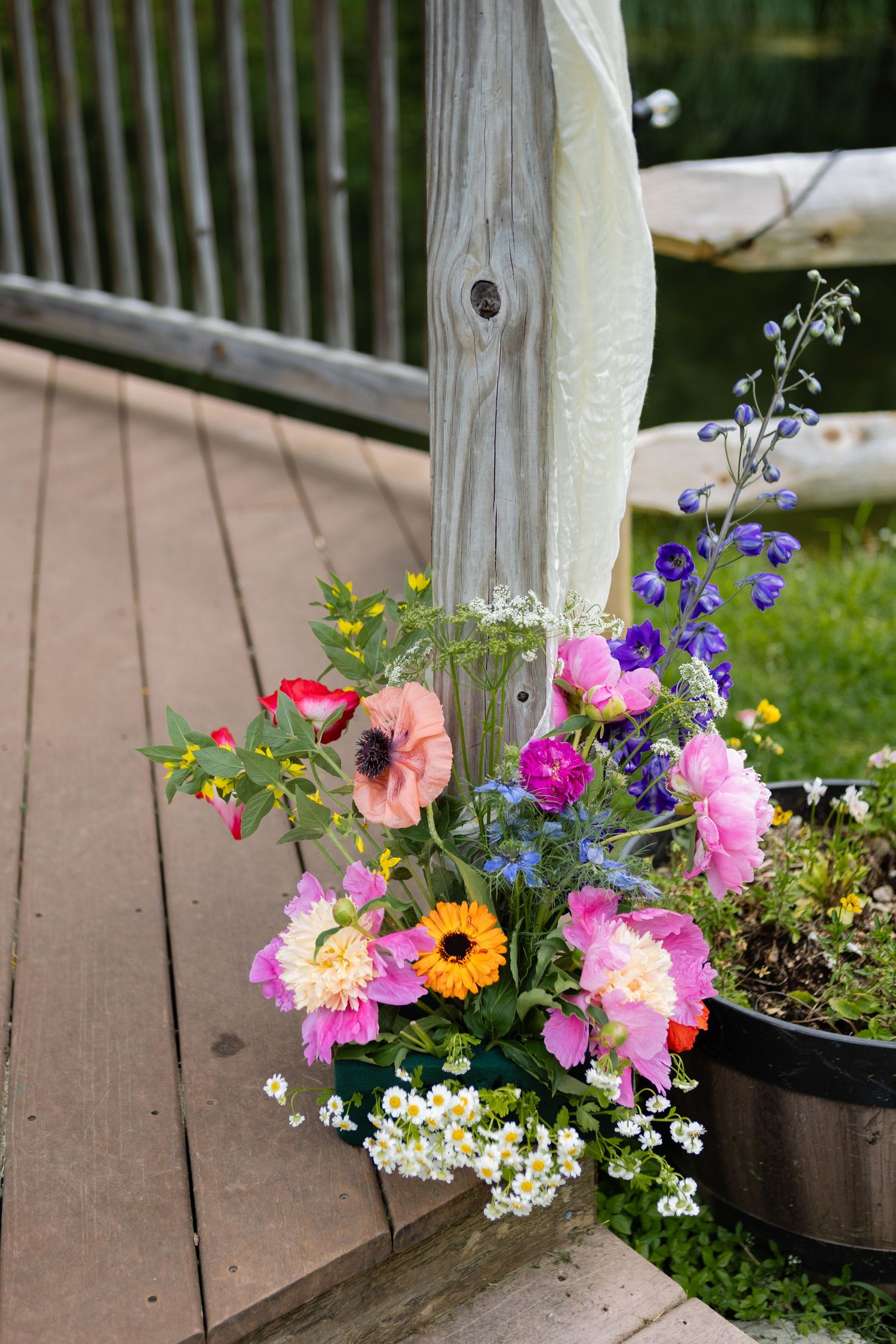 Colorful wildflower arrangement with pink and purple blooms on a wooden deck railing.