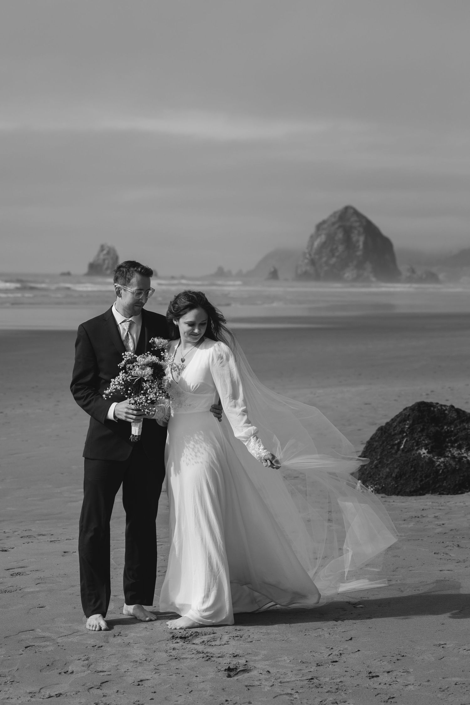 A romantic black and white beach wedding photoshoot with a couple posing against dramatic coastal scenery.
