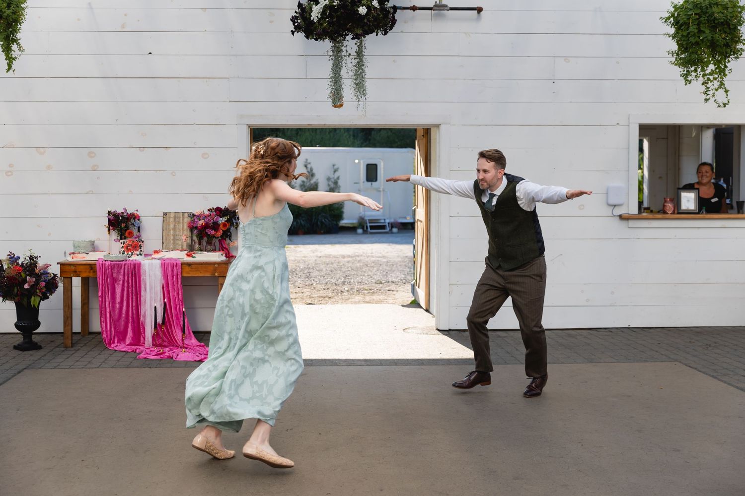 A couple dances together in a spacious room with white walls and wooden floors during what appears to be a dance lesson.