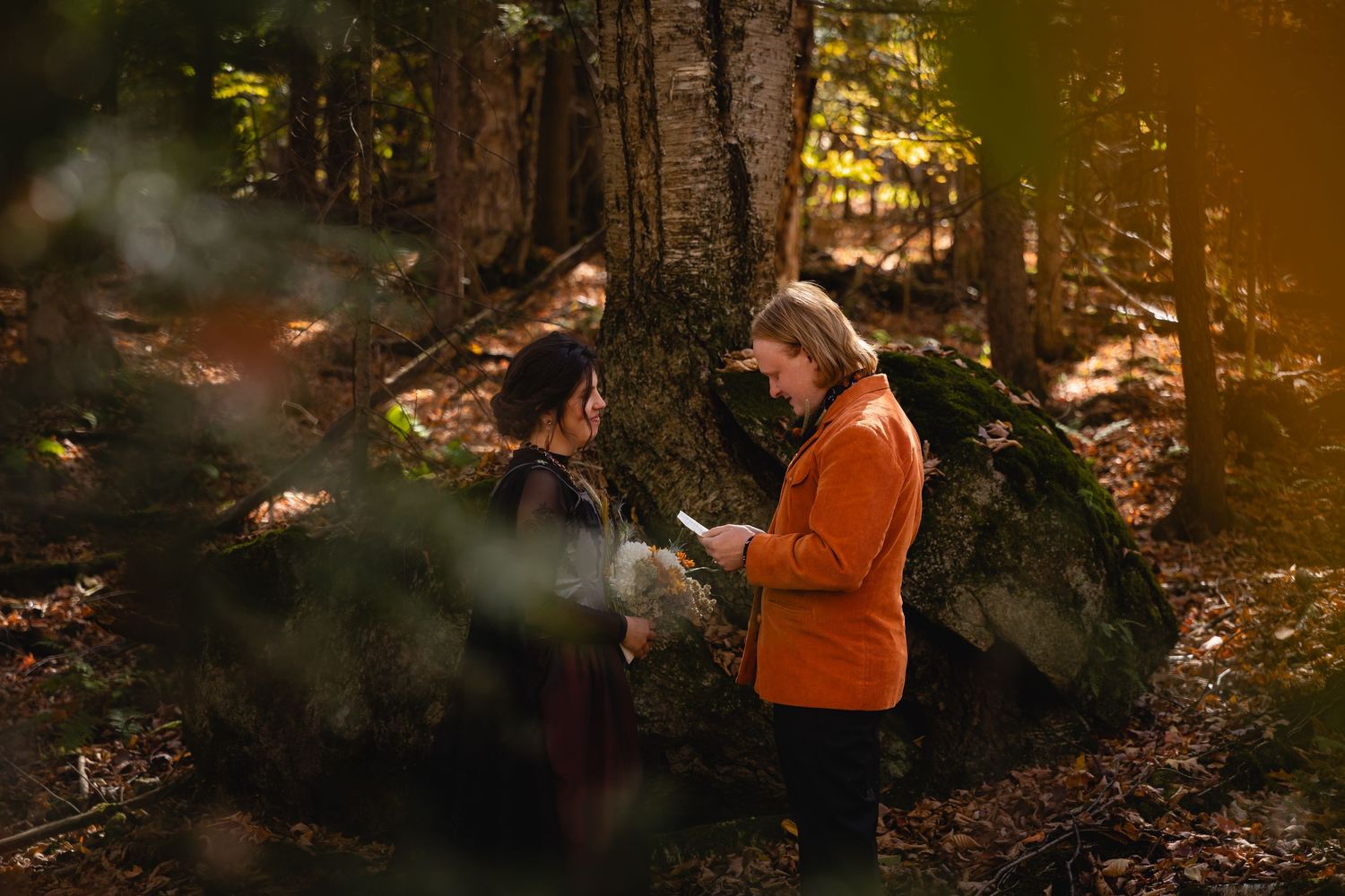 A person in an orange safety vest walks through a sunlit forest during autumn.