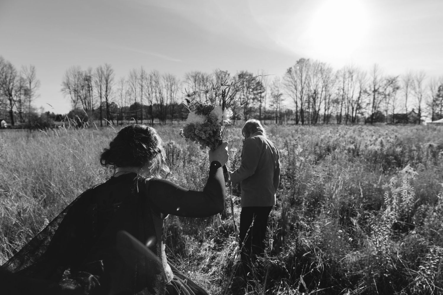 Black and white silhouettes of people walking through a field during sunset create a dramatic rural scene.