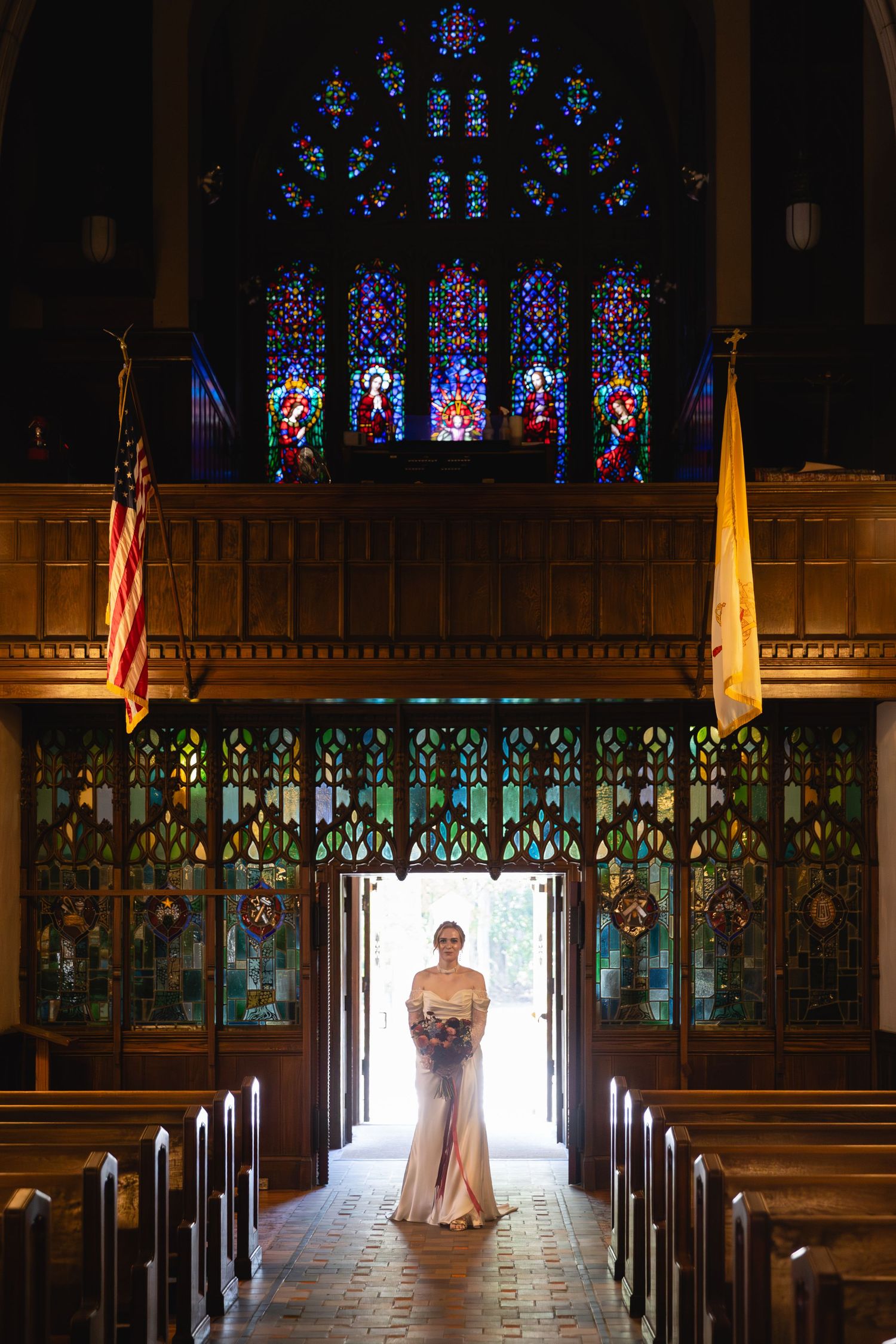Beautiful stained glass windows illuminate a church interior with wooden pews and ornate architectural details.