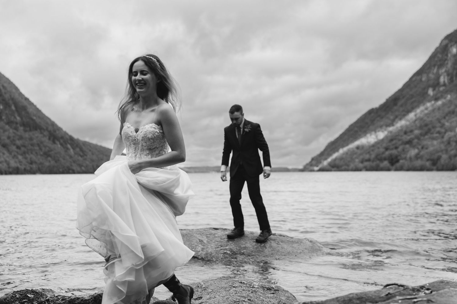 Black and white photo of wedding couple playing in mountain lake water.