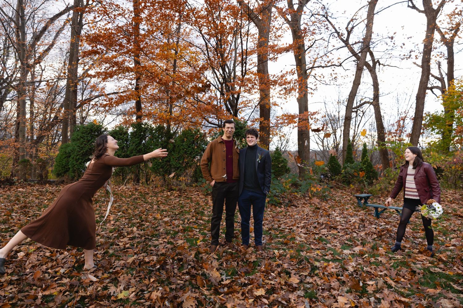 A dog jumps for a treat in a leaf-covered autumn forest as people enjoy the fall scene outdoors.