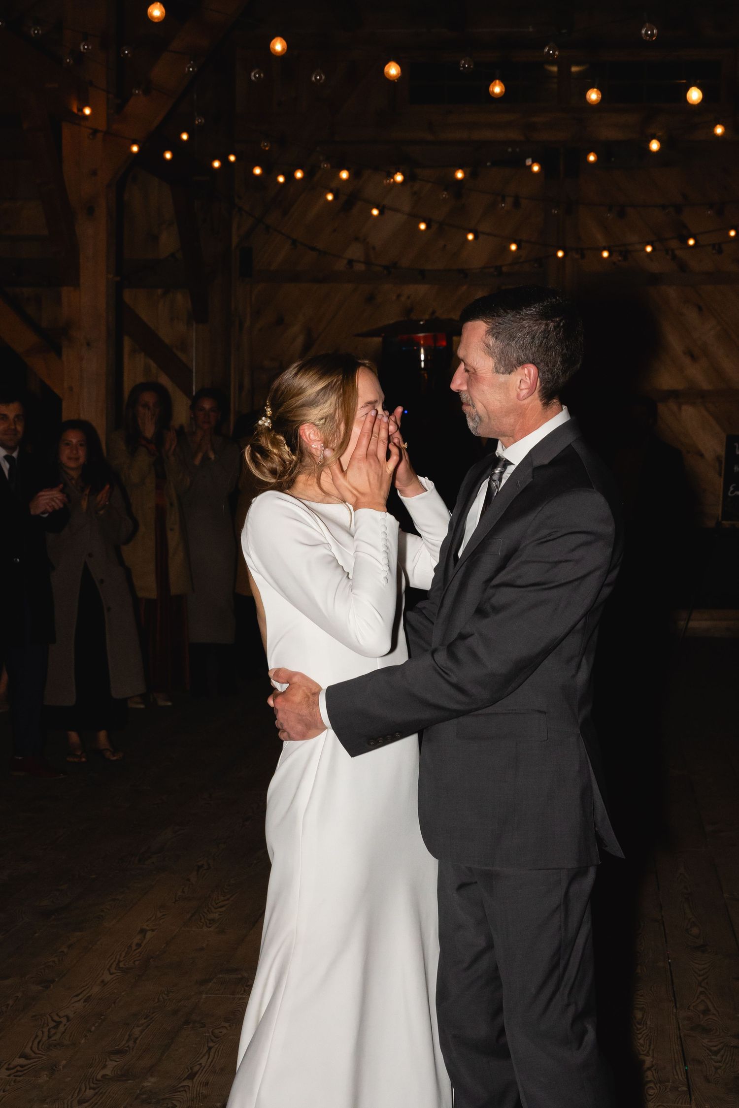 A couple shares an emotional moment while dancing under twinkling string lights at an evening wedding reception.