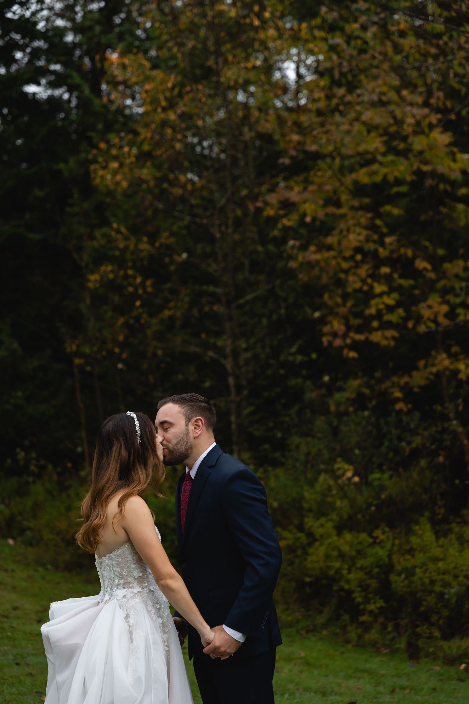 A tender wedding moment captured against autumn foliage in a garden setting.