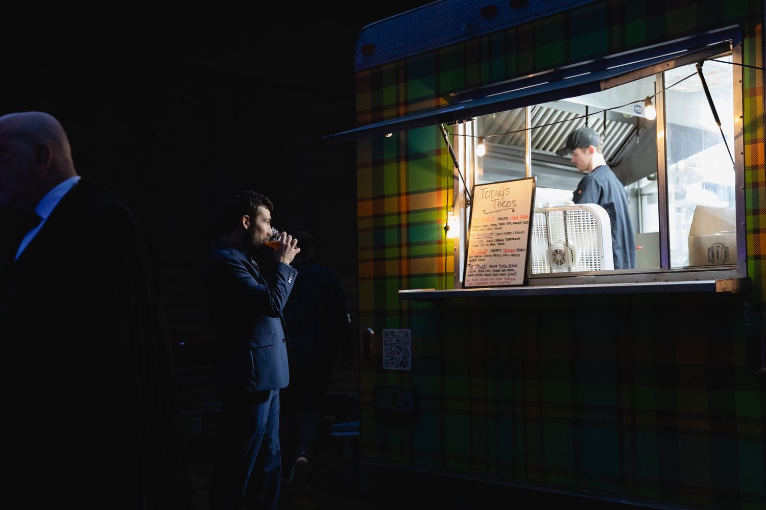 Wedding guest ordering food from a colorful tartan-patterned food truck at a nighttime reception.