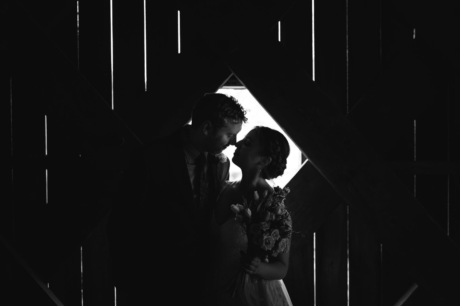 Romantic black and white silhouette of couple nearly kissing framed by barn doors.