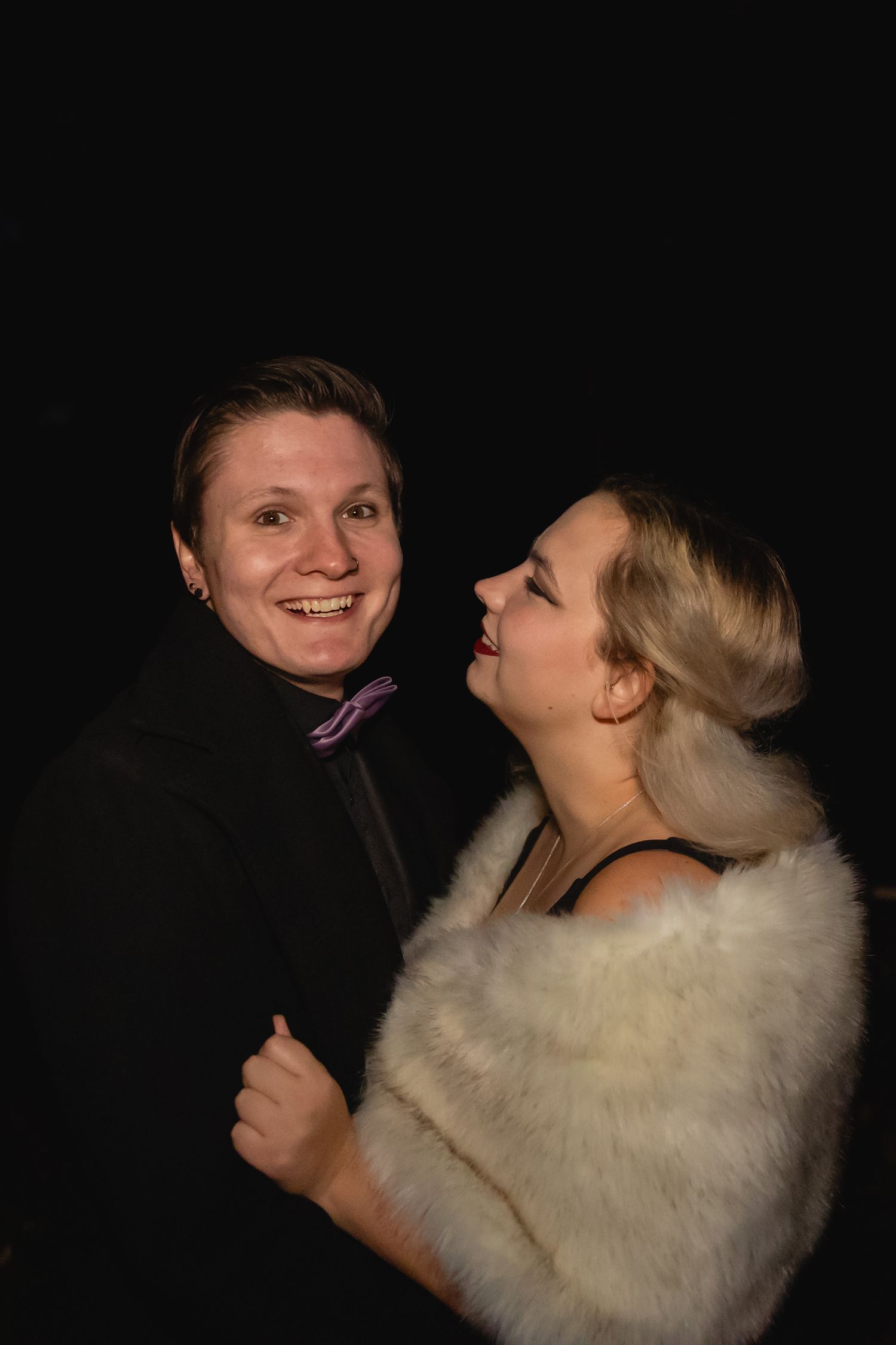 Smiling couple in formal attire posing together against a black background at a night event.