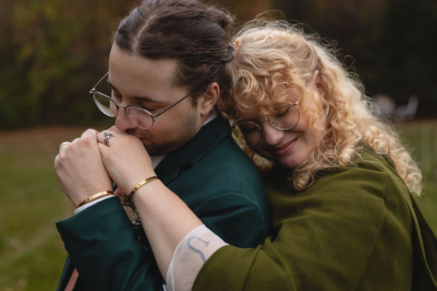 Two people share emotional embrace outdoors wearing green and teal sweaters.