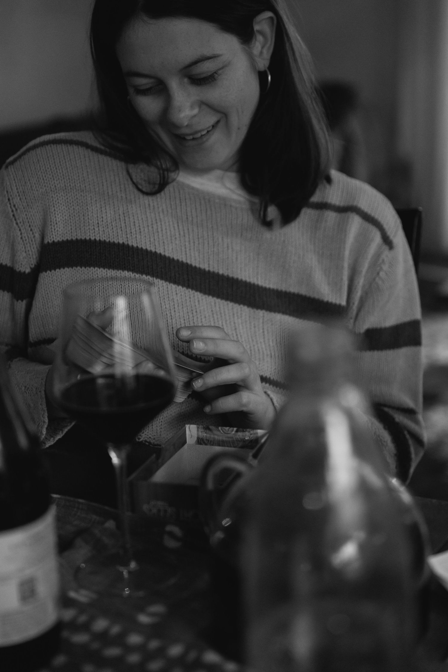 A candid black and white photo showing someone in a striped sweater smiling while holding a glass of red wine.