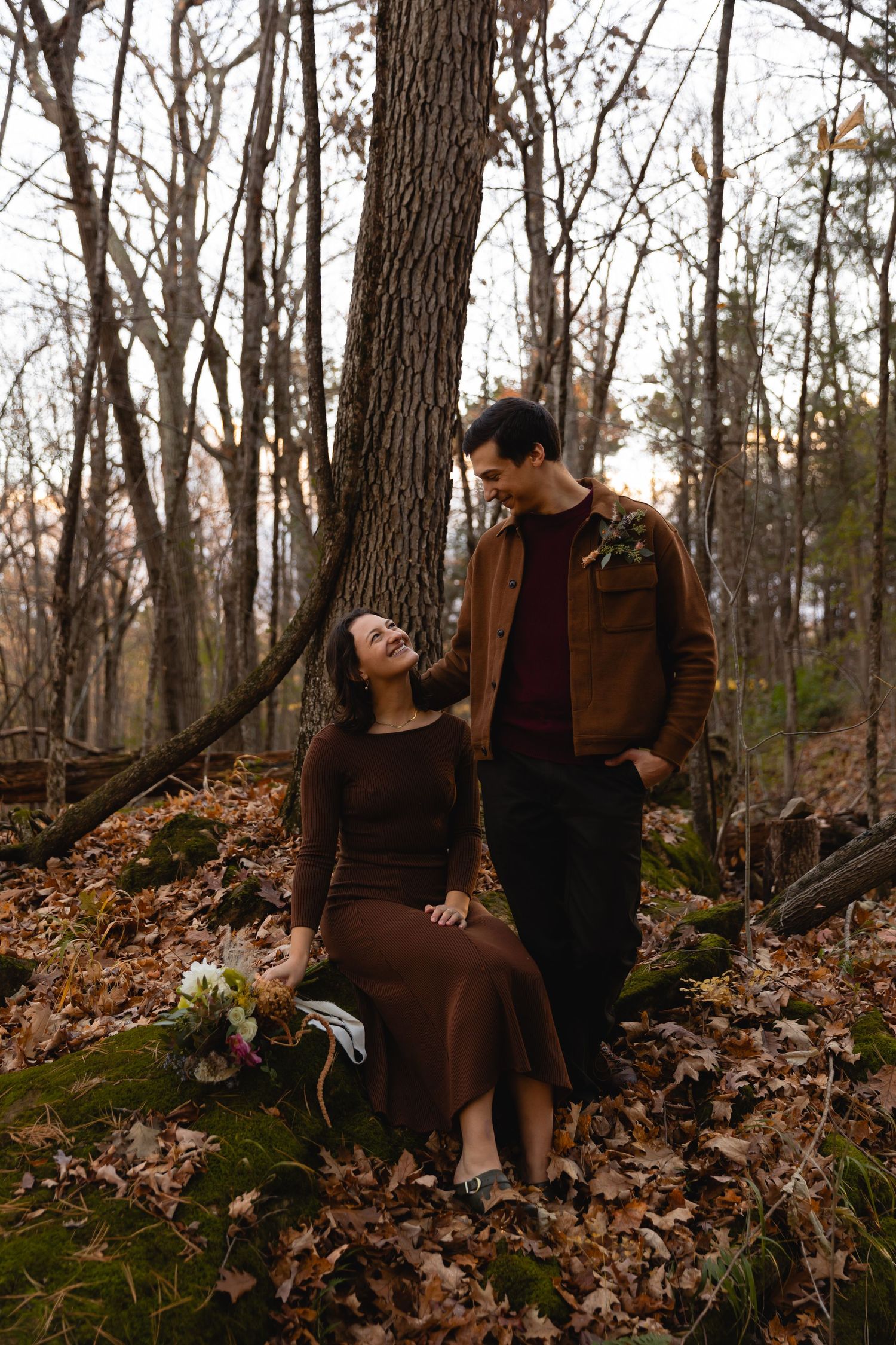 A romantic autumn forest scene with a couple sharing a tender moment among fallen leaves and tall trees.