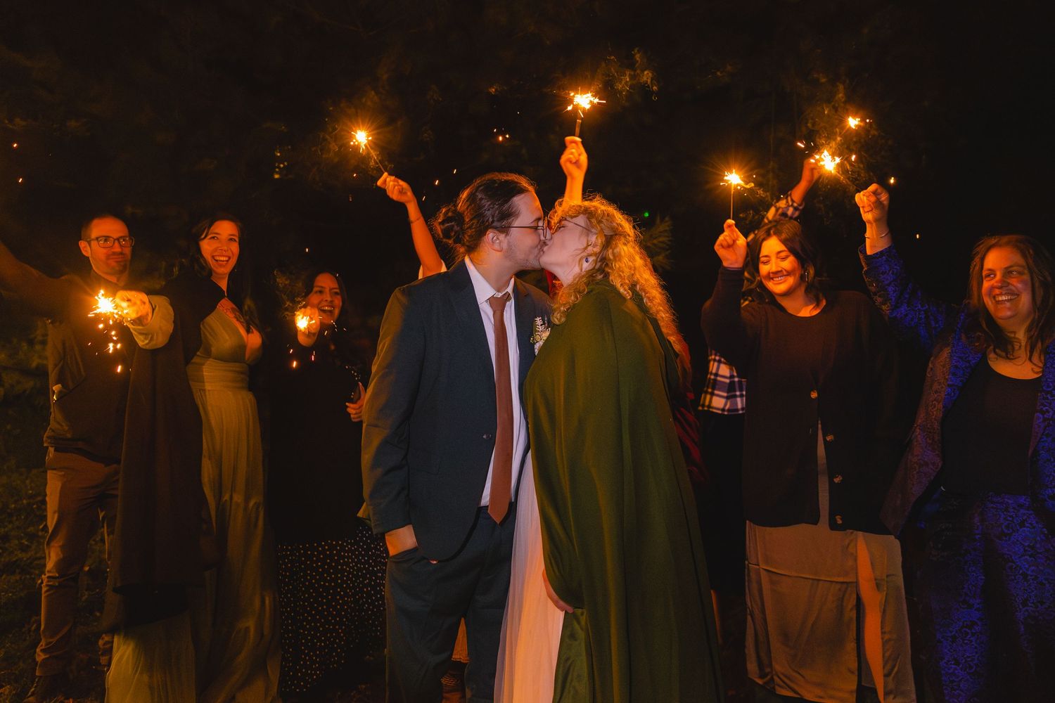 Wedding celebration with sparklers at night surrounded by guests.