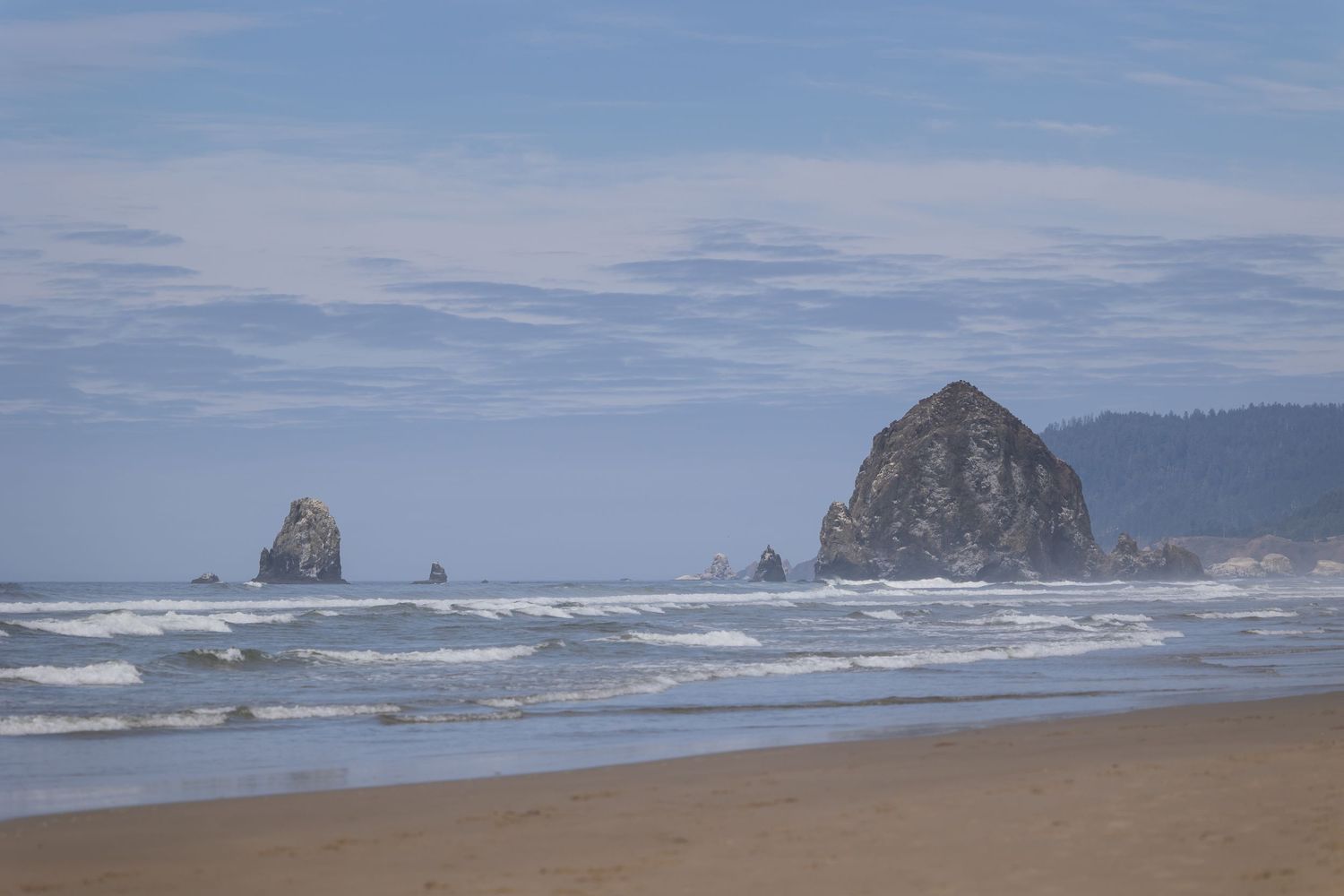 Panoramic view of Cannon Beach in Oregon showing Haystack Rock and coastal cliffs along the misty Pacific shoreline.