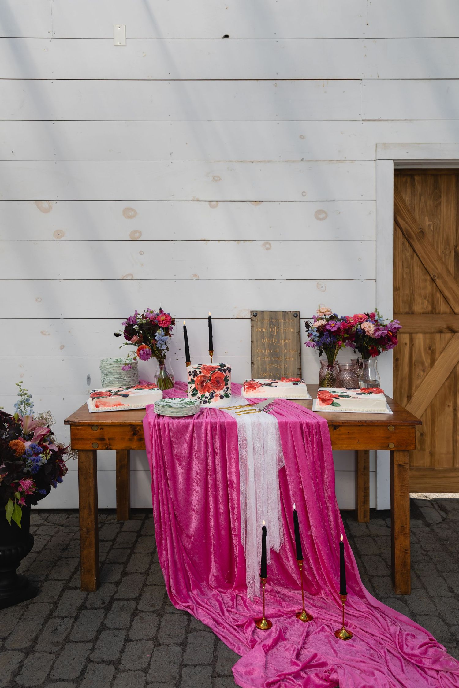 A rustic table decorated with pink velvet fabric, floral arrangements, and place settings against a white shiplap wall.