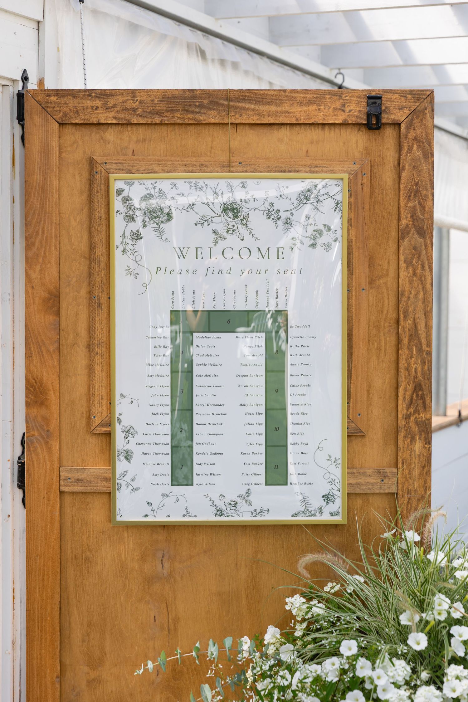 Wedding welcome signs and seating charts displayed on wooden doors with white floral decorations.
