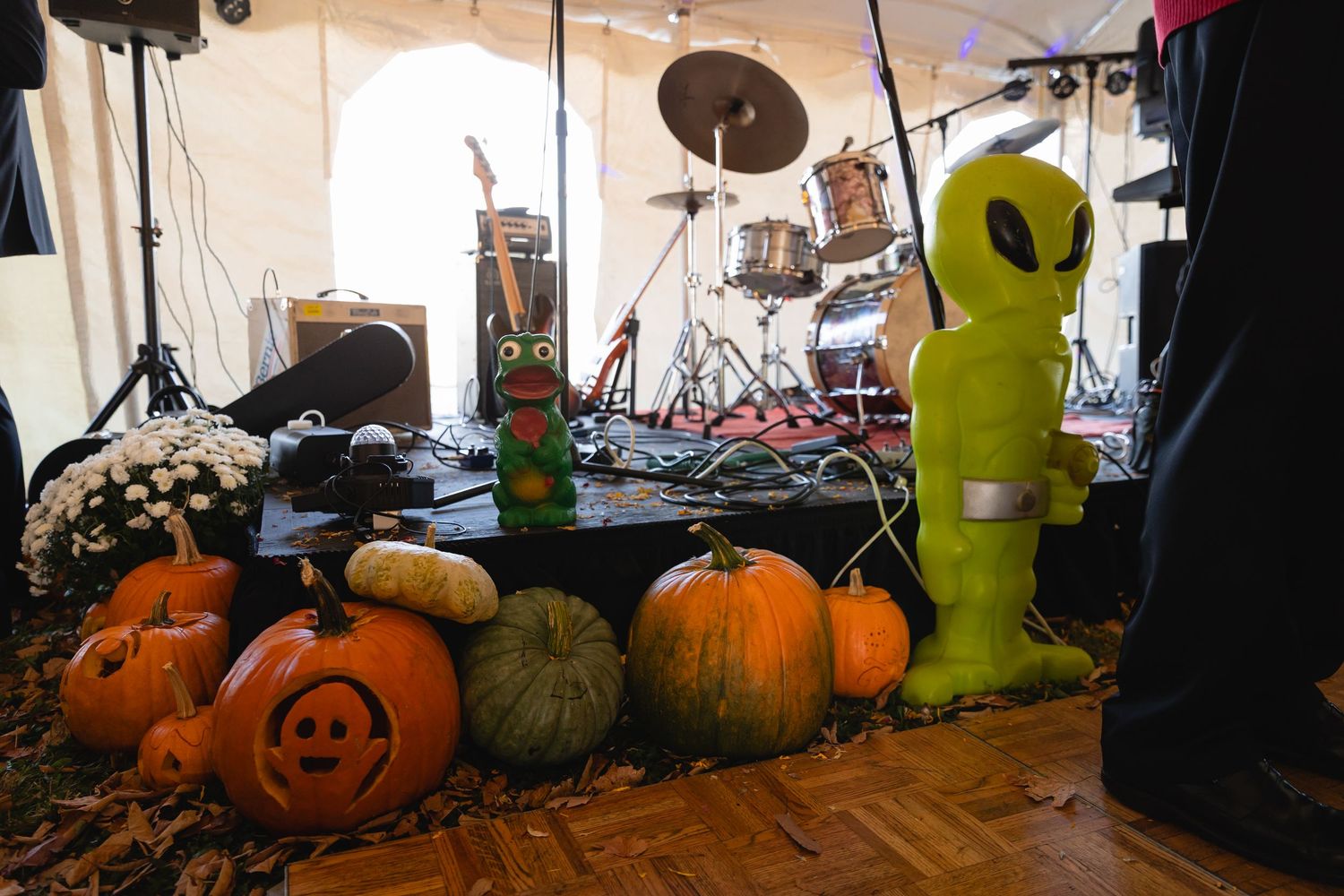 Halloween decorations including pumpkins, carved jack-o-lanterns and an inflatable alien figure set up near a drum kit on stage.