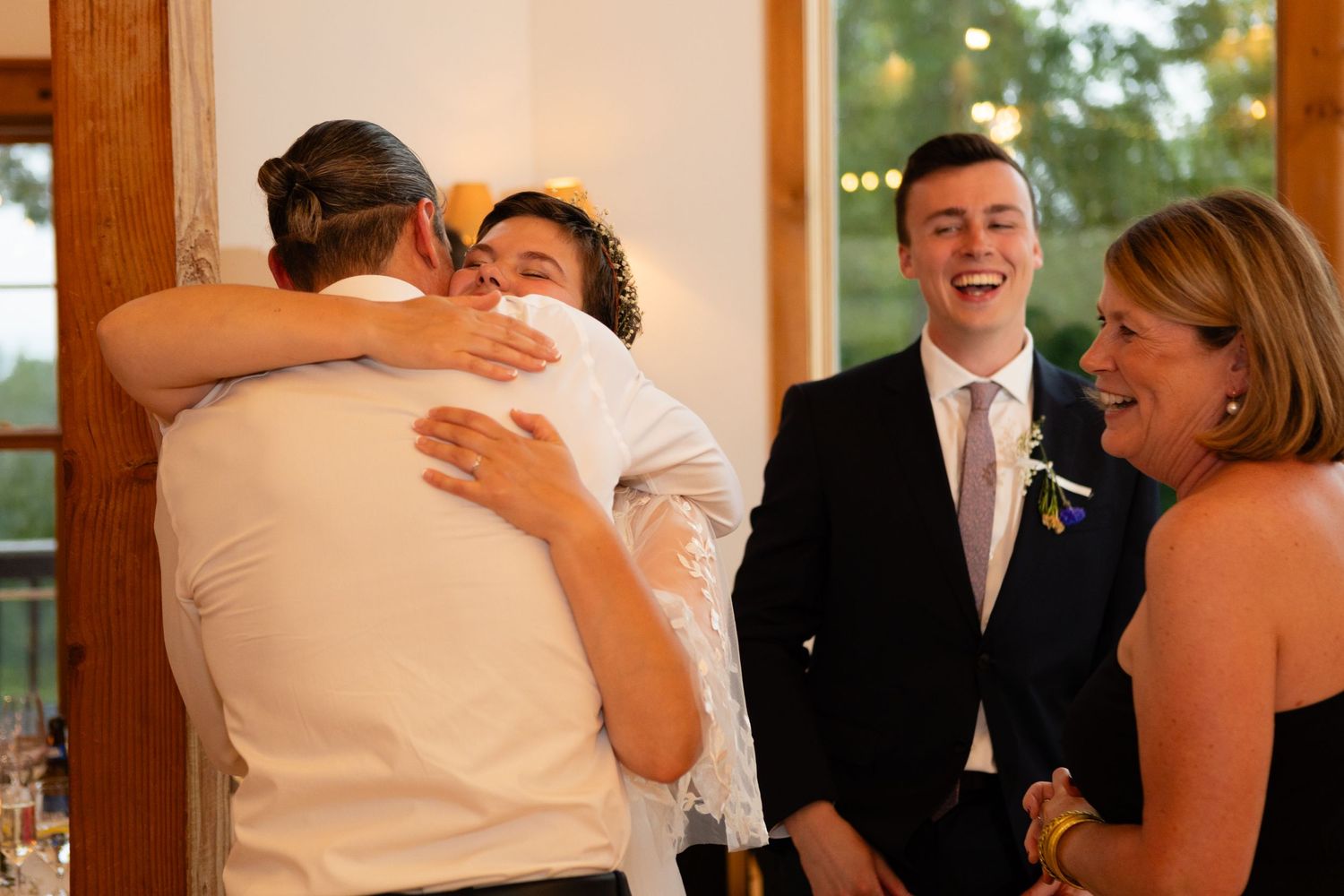 Guests share warm embraces and laughter during a heartfelt wedding reception moment.