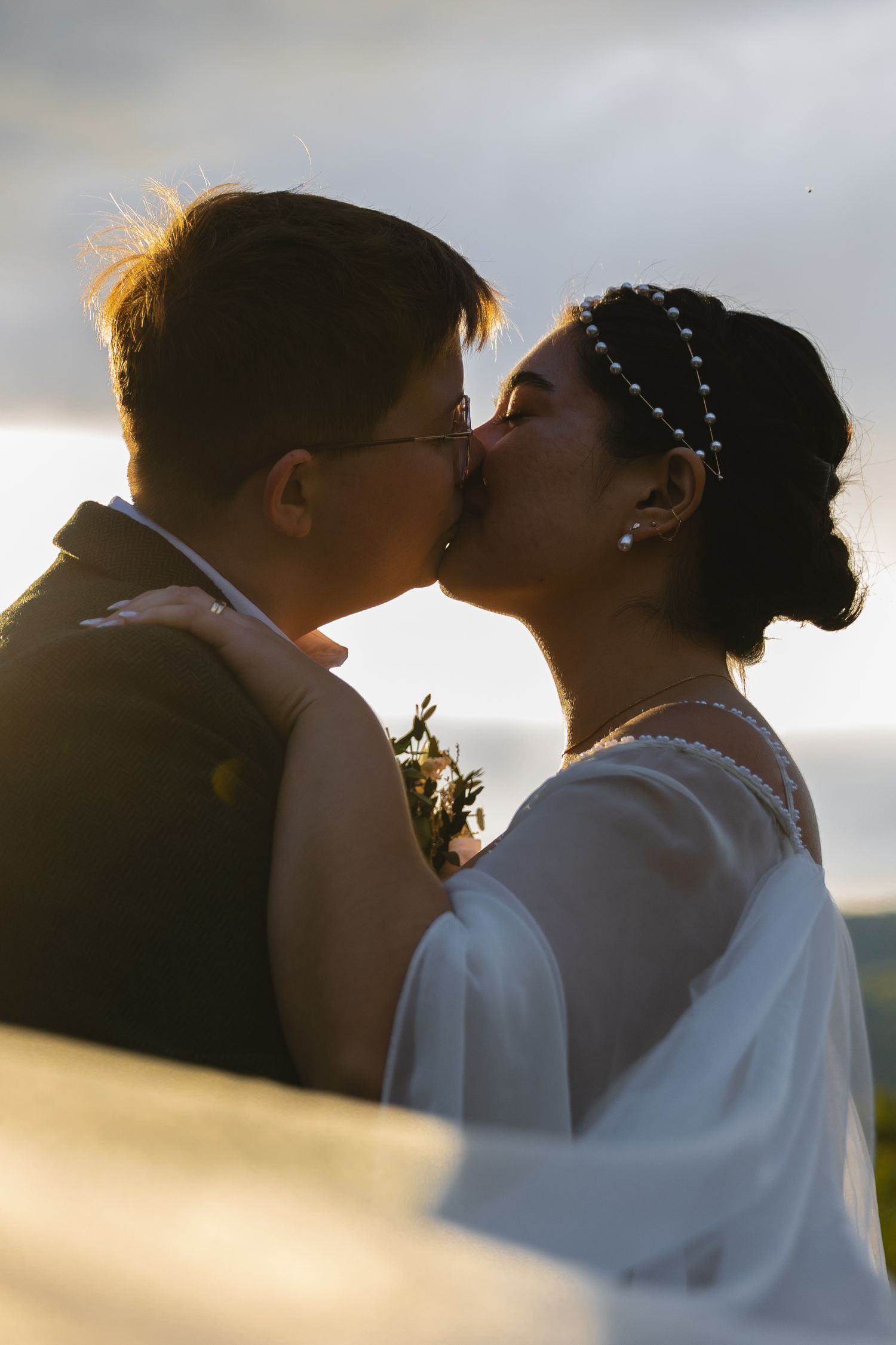 Sunset silhouette of a wedding couple sharing a tender kiss with golden light behind them.
