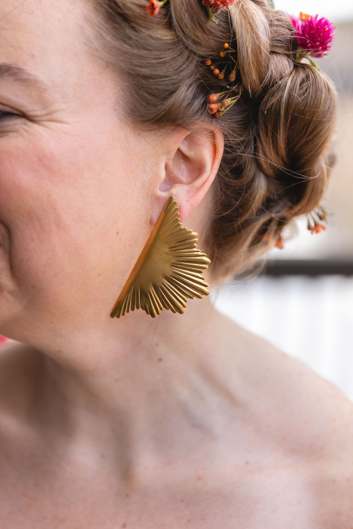 Gold fan-shaped statement earring paired with floral hair accessories.