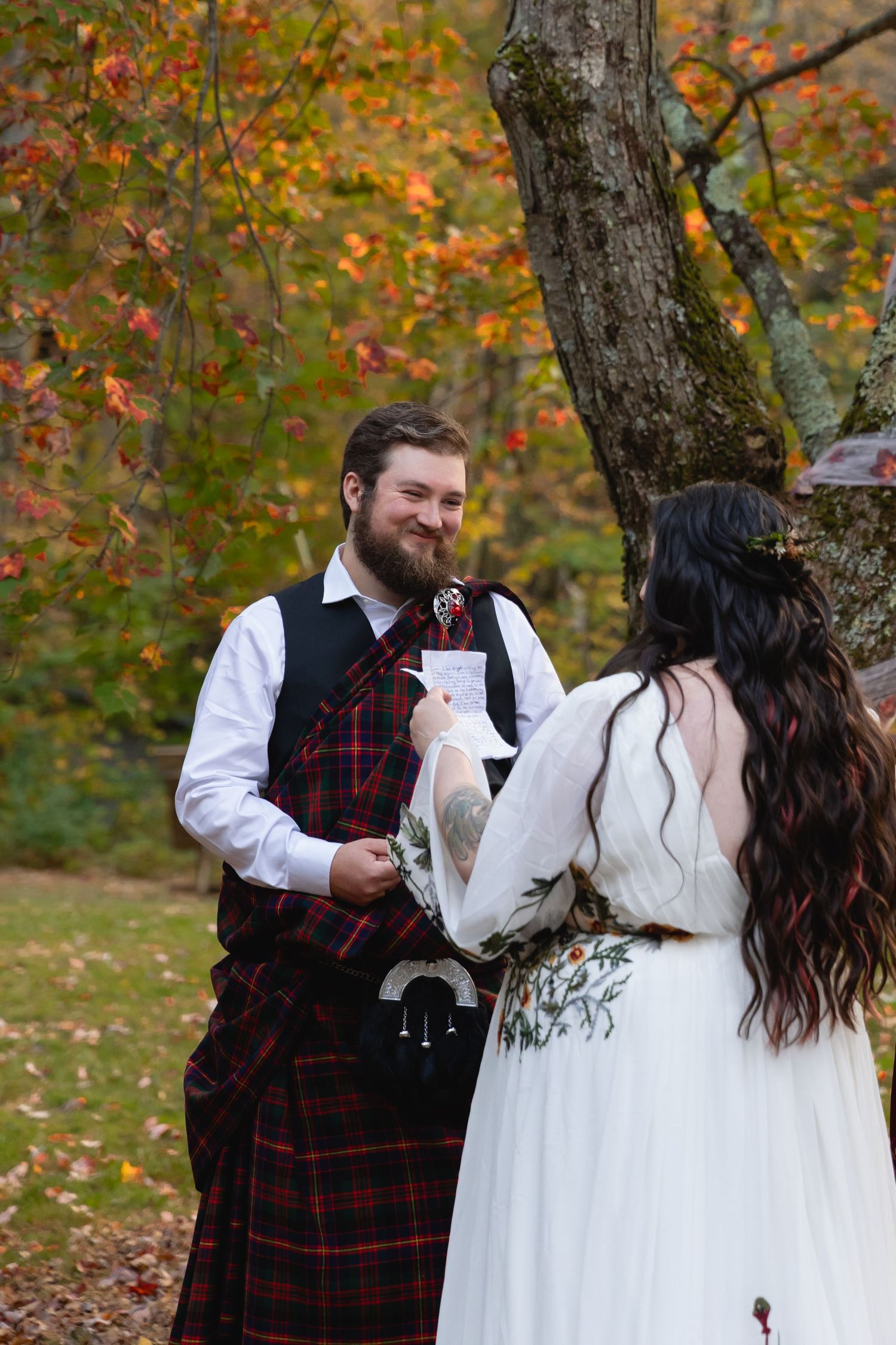 A couple in Scottish wedding attire shares a moment amid fall foliage.