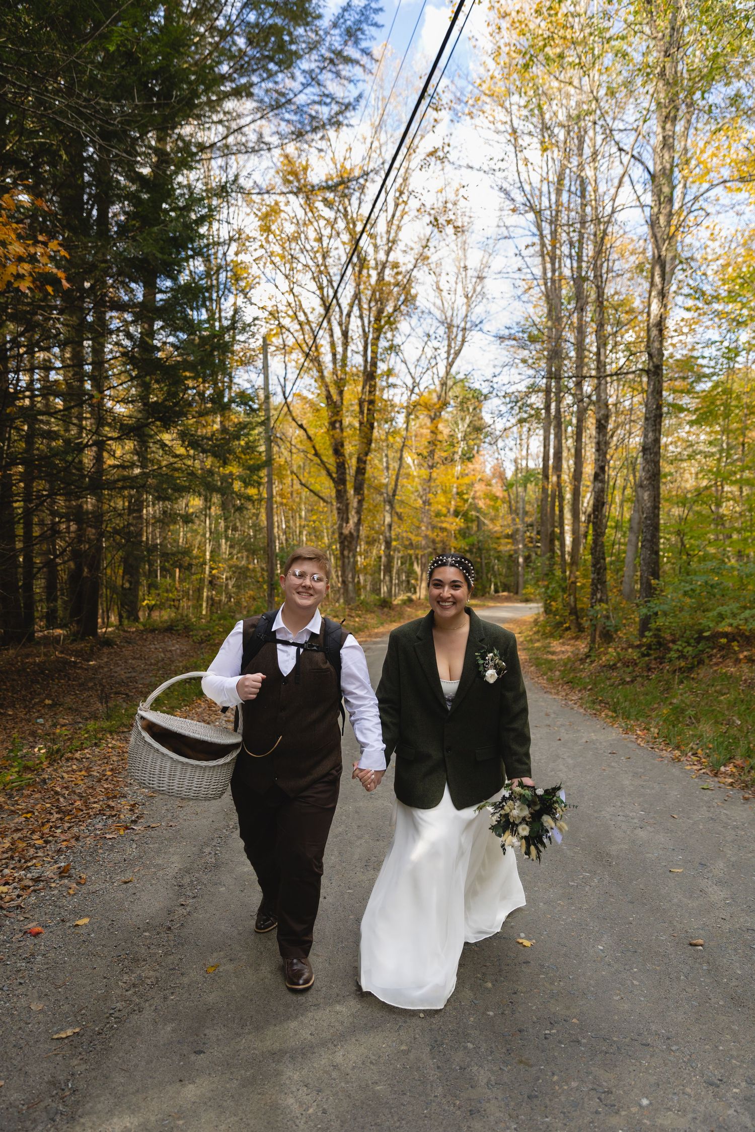 A couple walking hand in hand down a forest path surrounded by fall foliage.