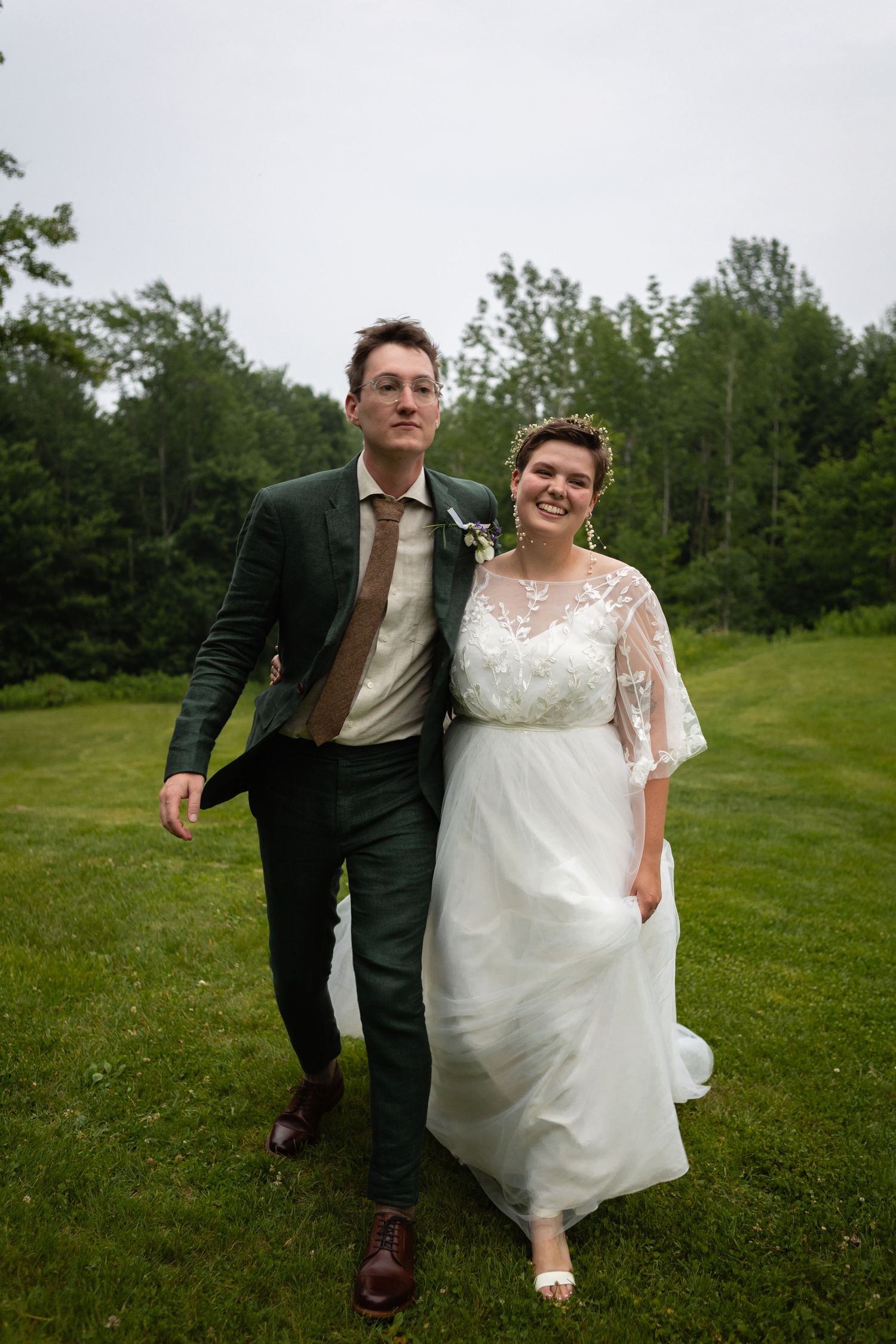 A couple walks together on a lush green lawn during their wedding celebration.