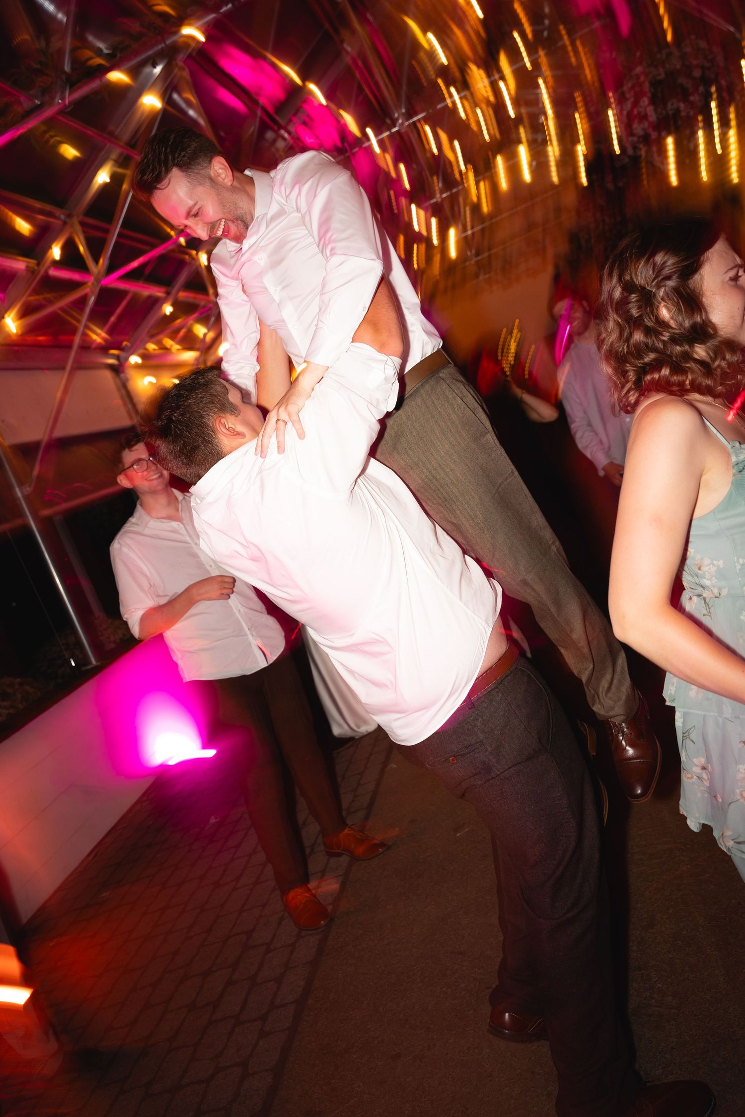 Couples dancing in a dimly lit venue with dramatic pink and purple lighting creating a festive atmosphere.