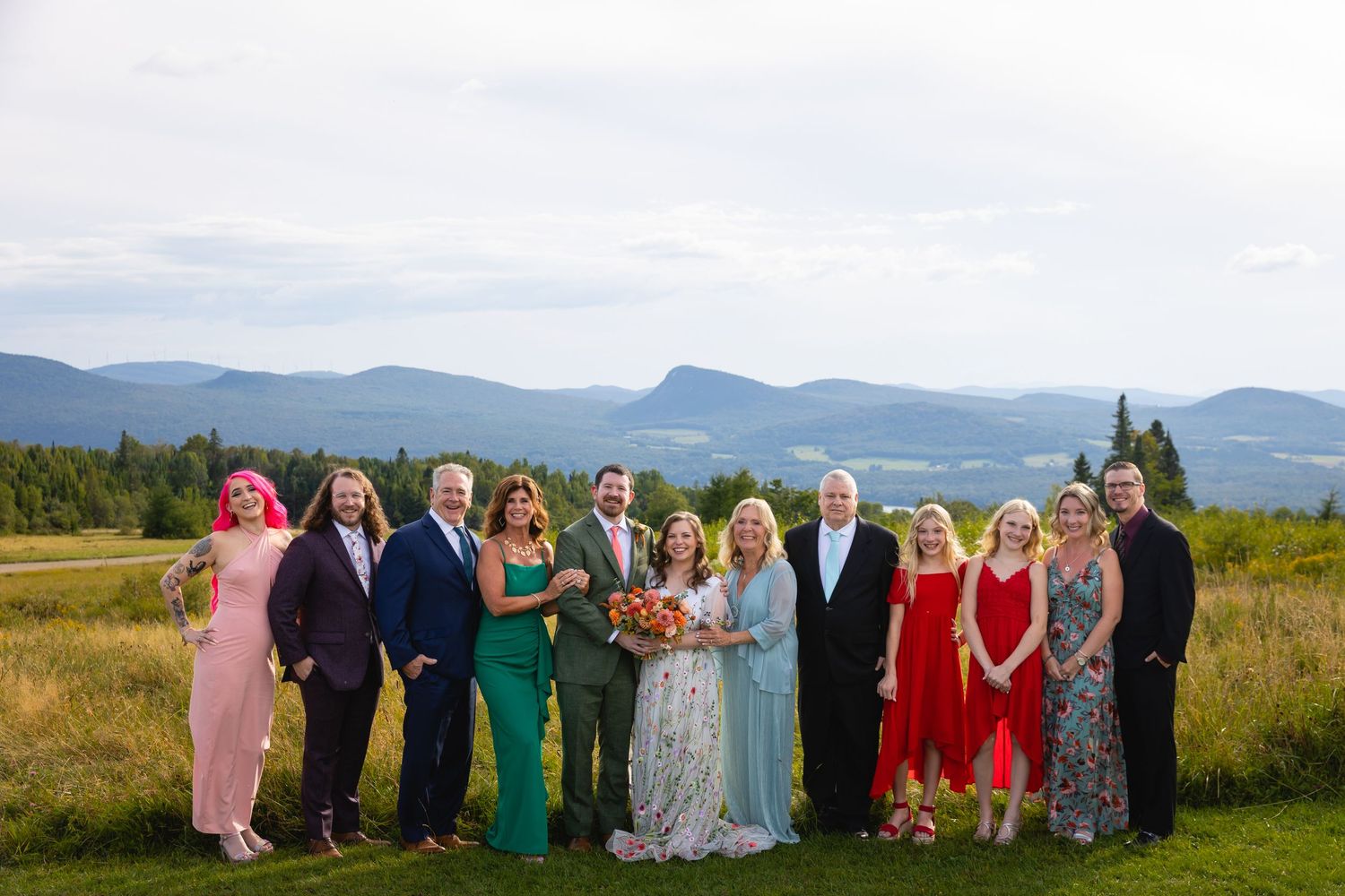 Wedding party stands together on a hilltop with scenic mountain views and golden fields in the background.
