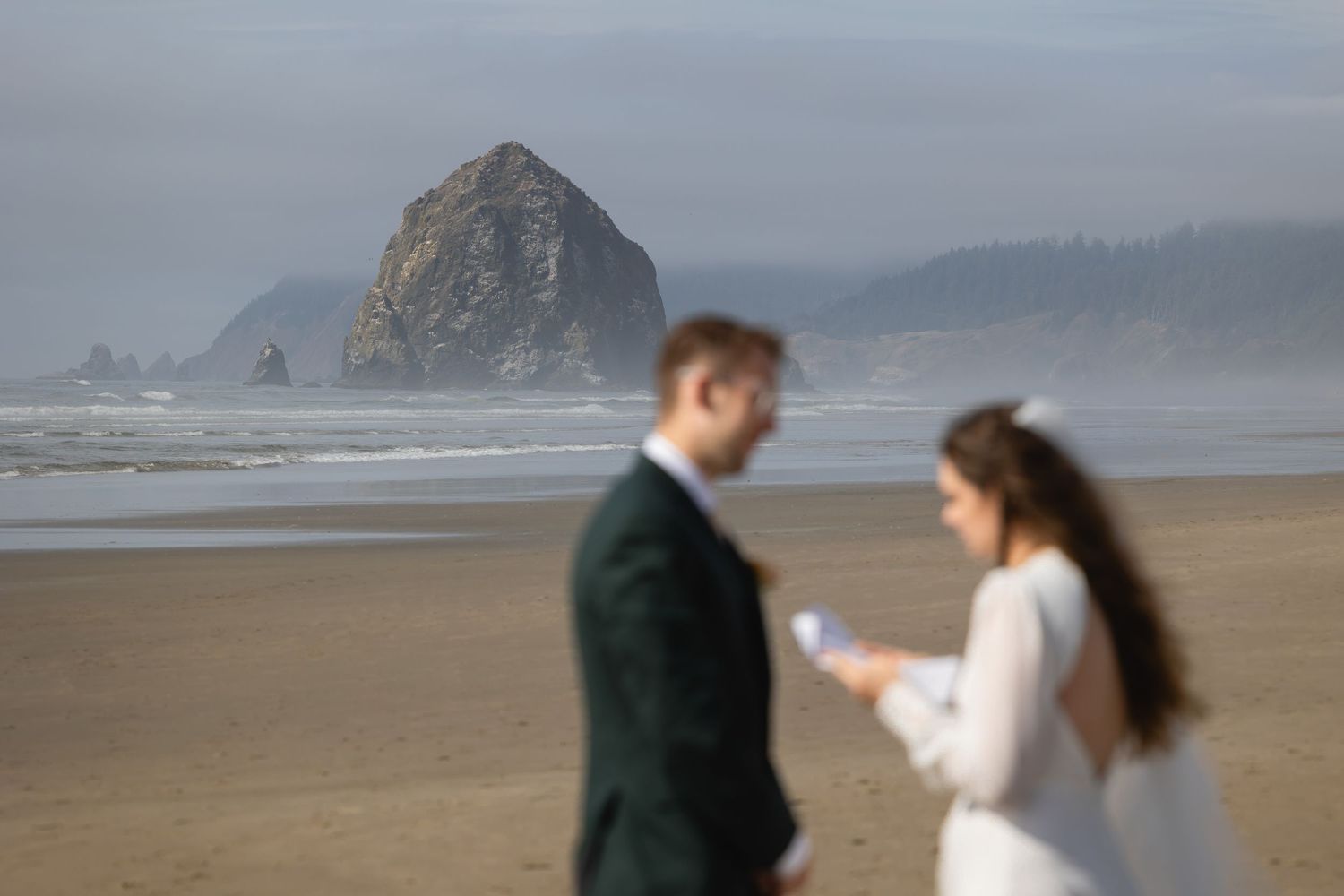A couple dances together on a misty beach with dramatic coastal rock formations in the background.
