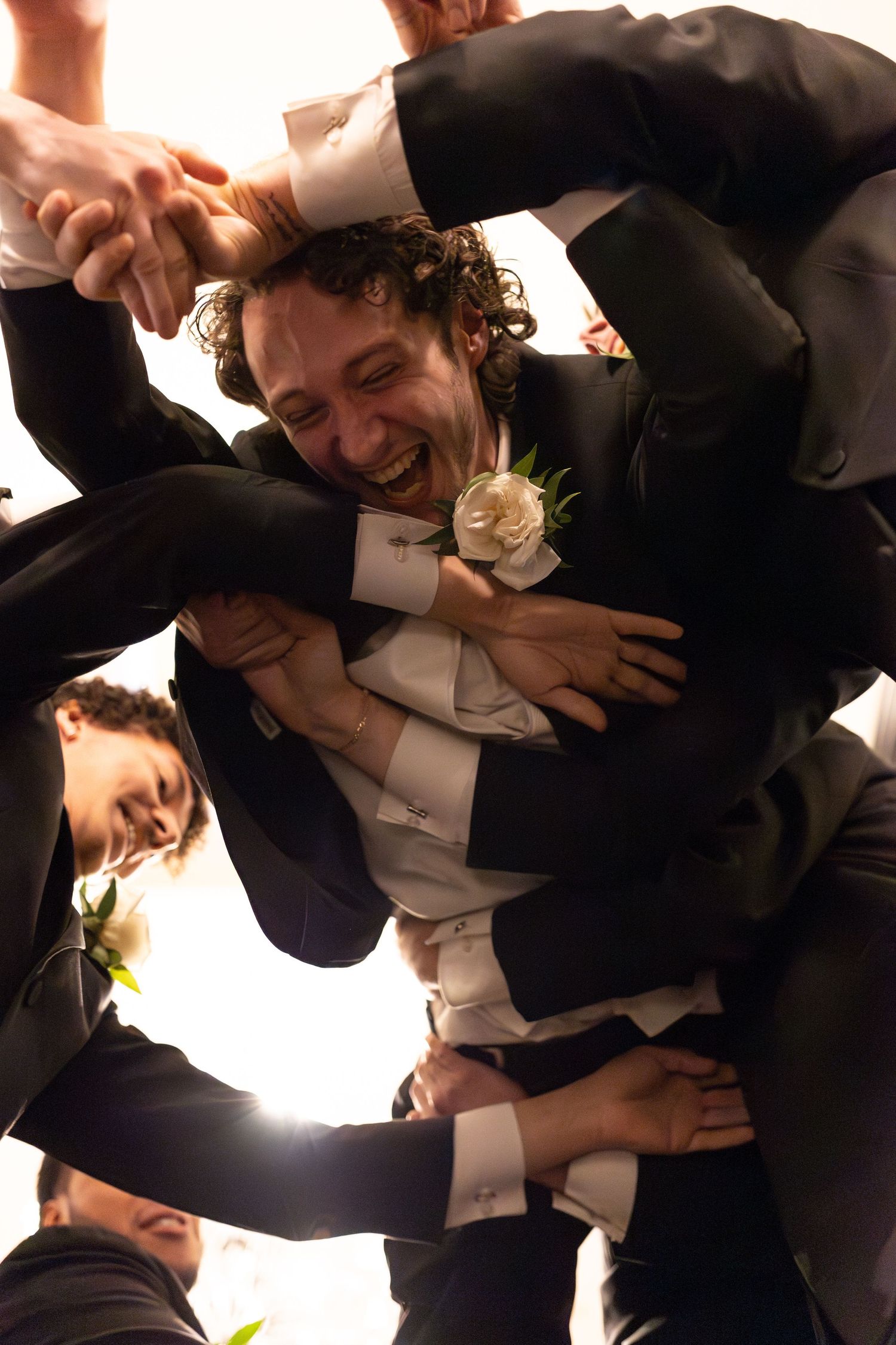 Laughter and joy as a tuxedo-clad celebrant is hoisted by friends at a formal gathering.