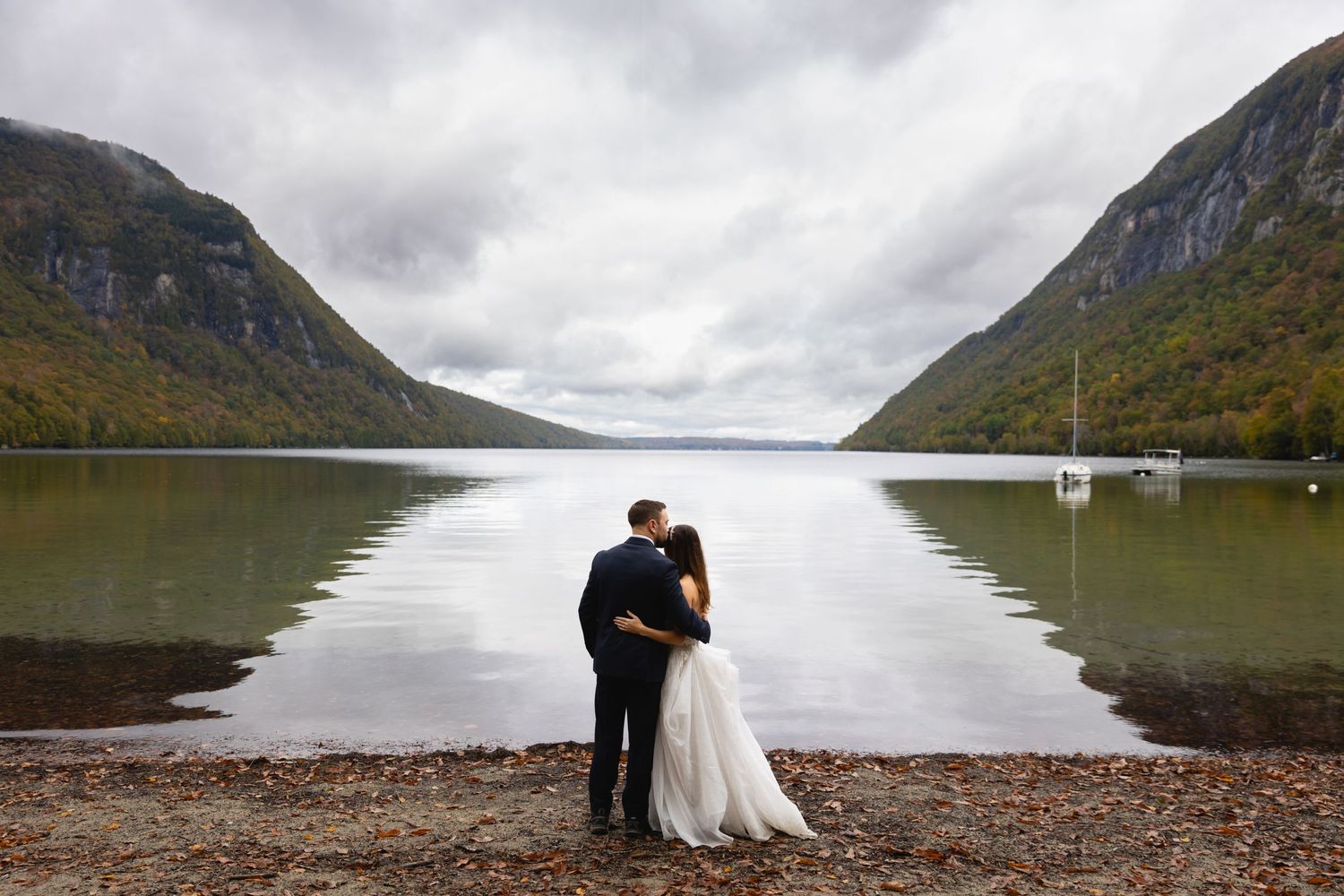 Wedding couple stands at lakeside with dramatic mountain valley views.
