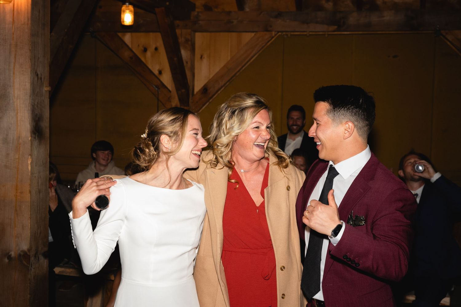 Guests celebrating at an indoor wedding reception with wooden beams and warm lighting.