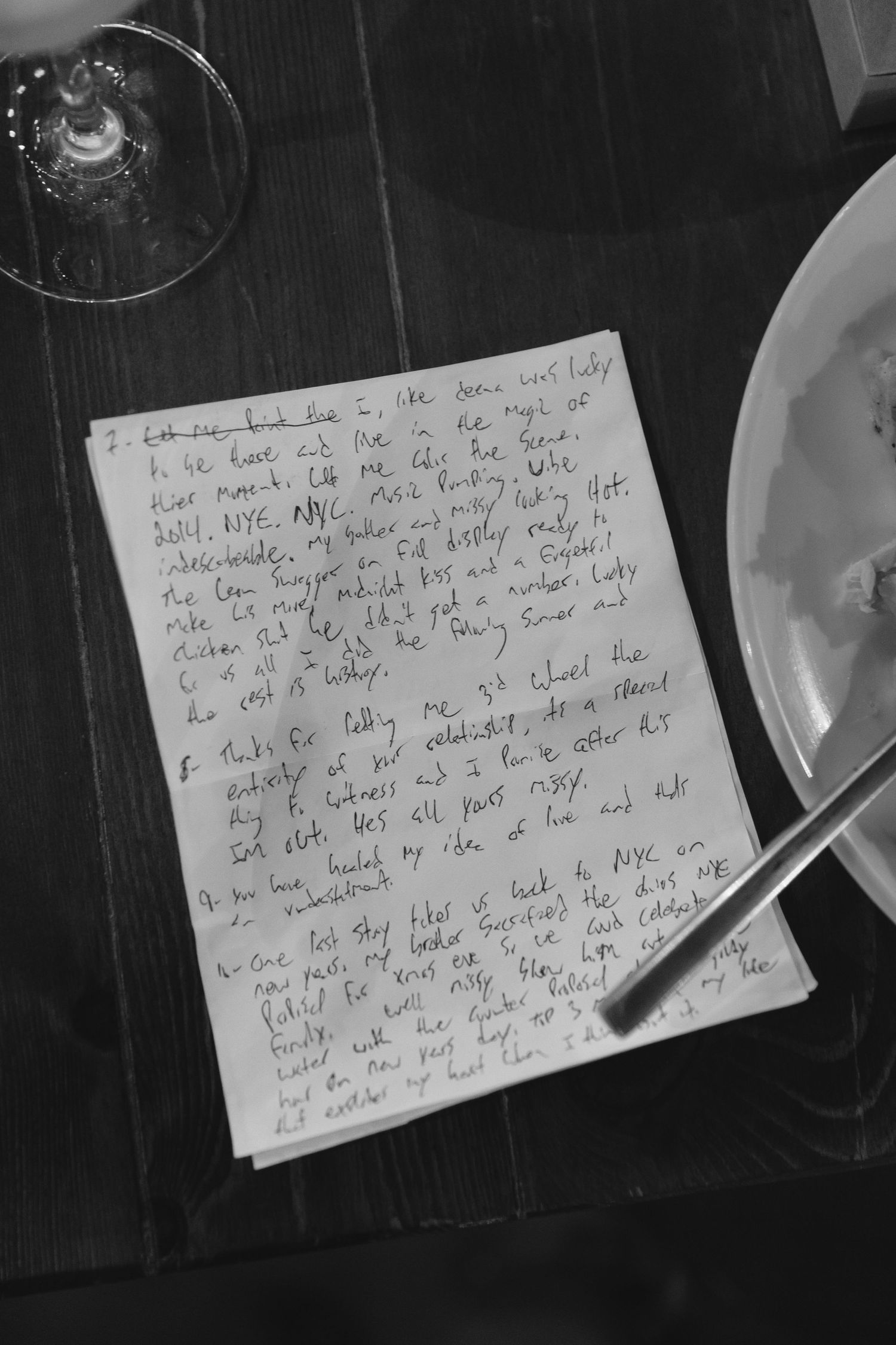 A handwritten note with romantic wedding vows sits on a dark wooden table next to a wine glass.