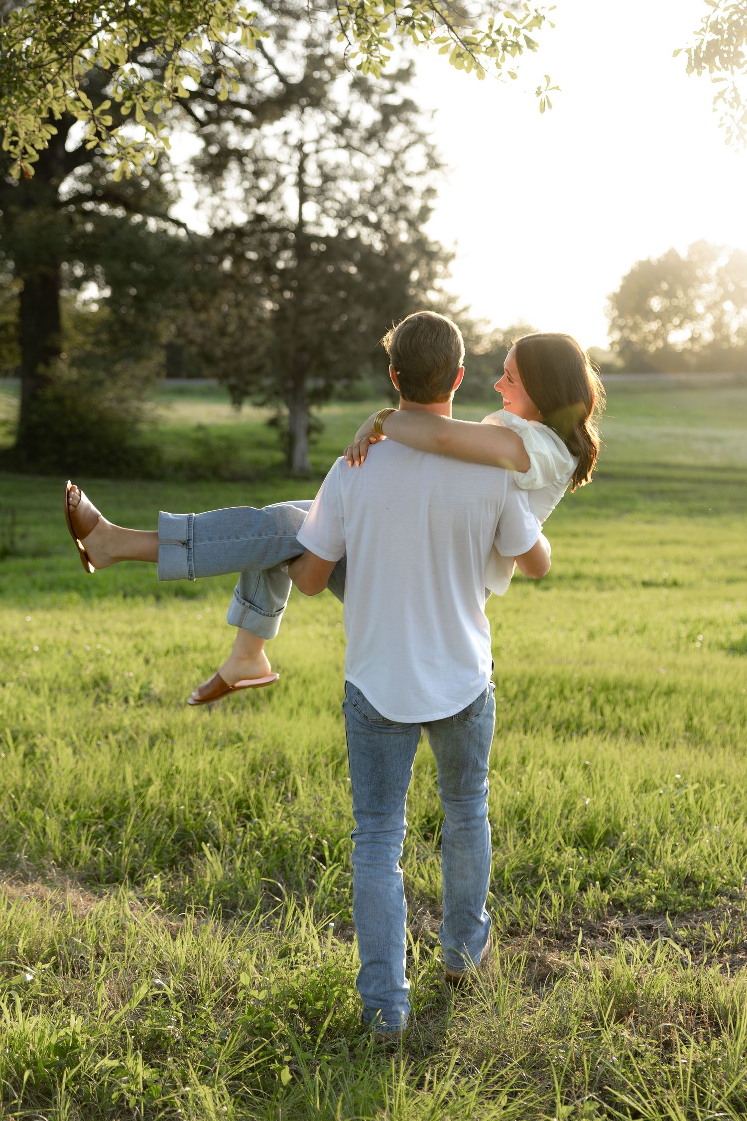 Romantic couple photos in a natural grass field setting with large trees at sunset.