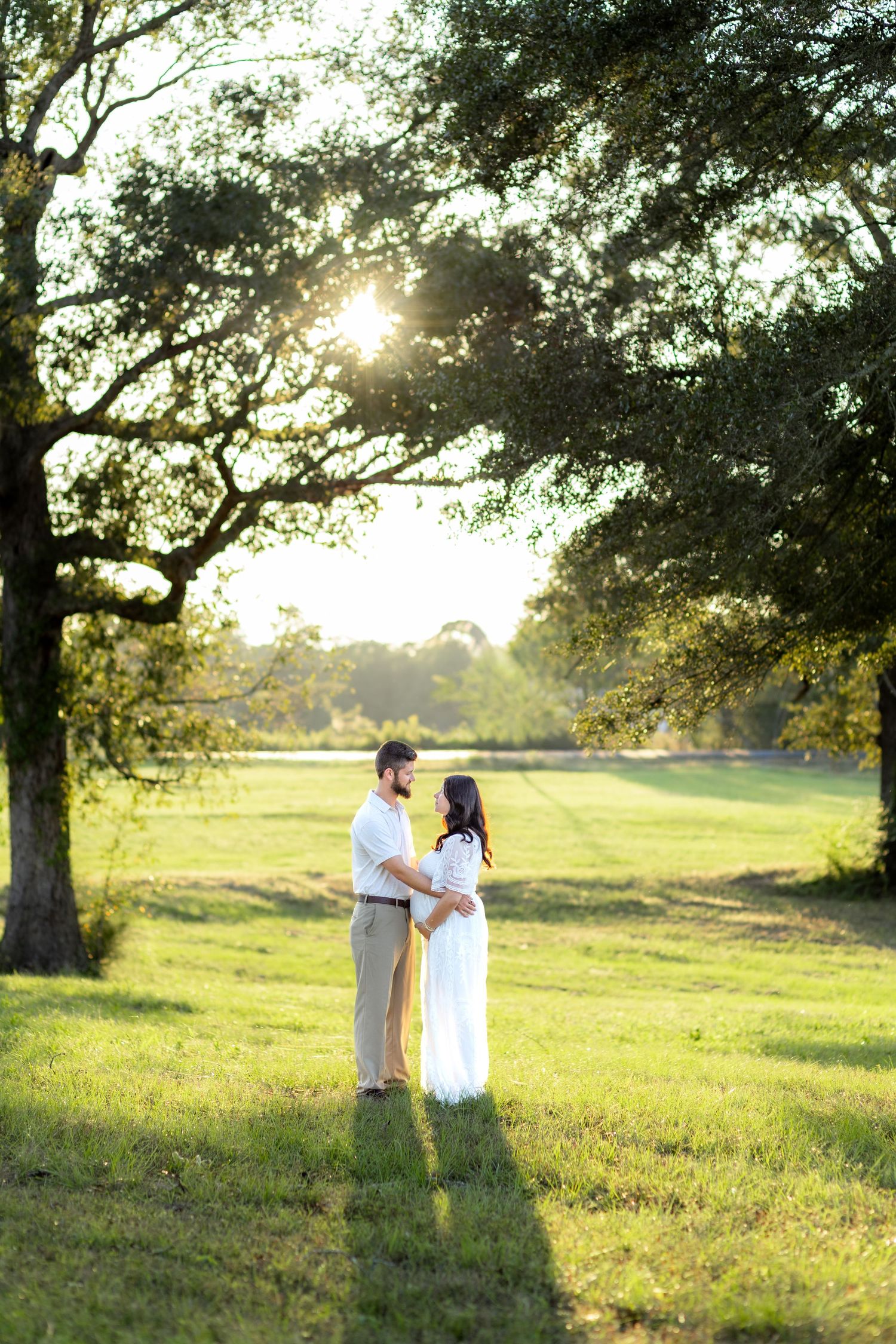 Expecting couple holding each other in a grass field at sunset in Dothan, Alabama