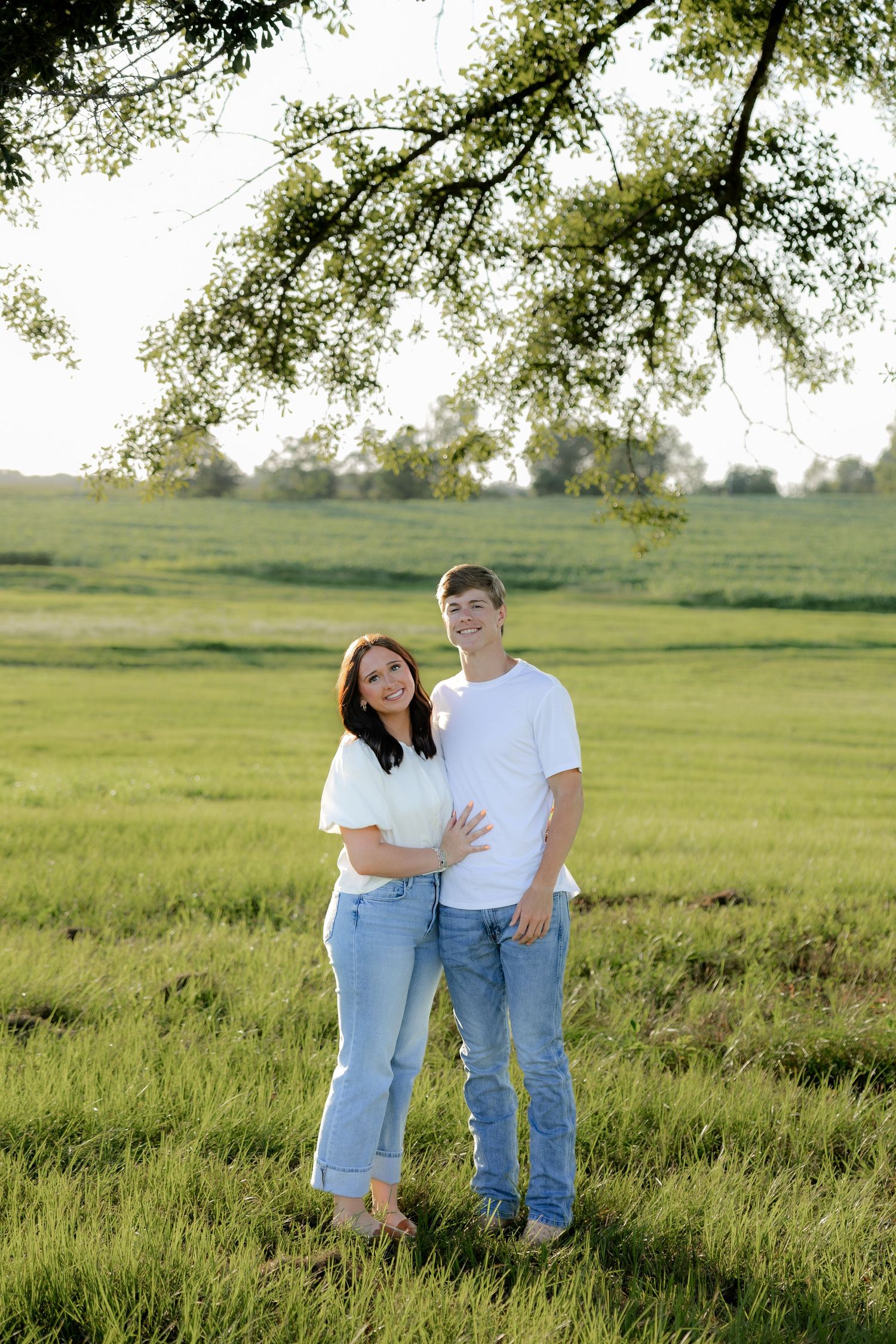 Romantic couple photos in a natural grass field setting with large trees at sunset.