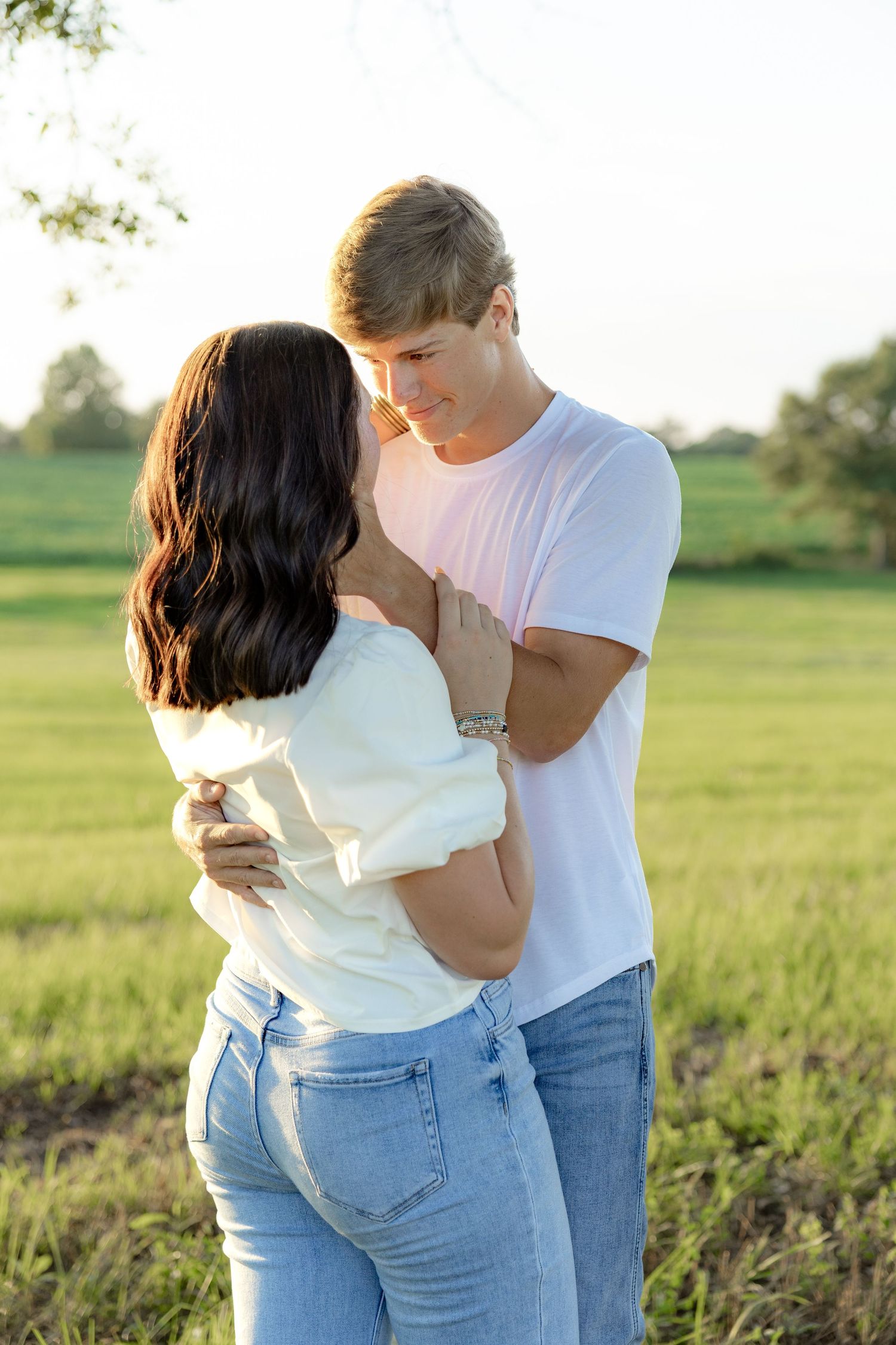 Romantic couple photos in a natural grass field setting with large trees at sunset.