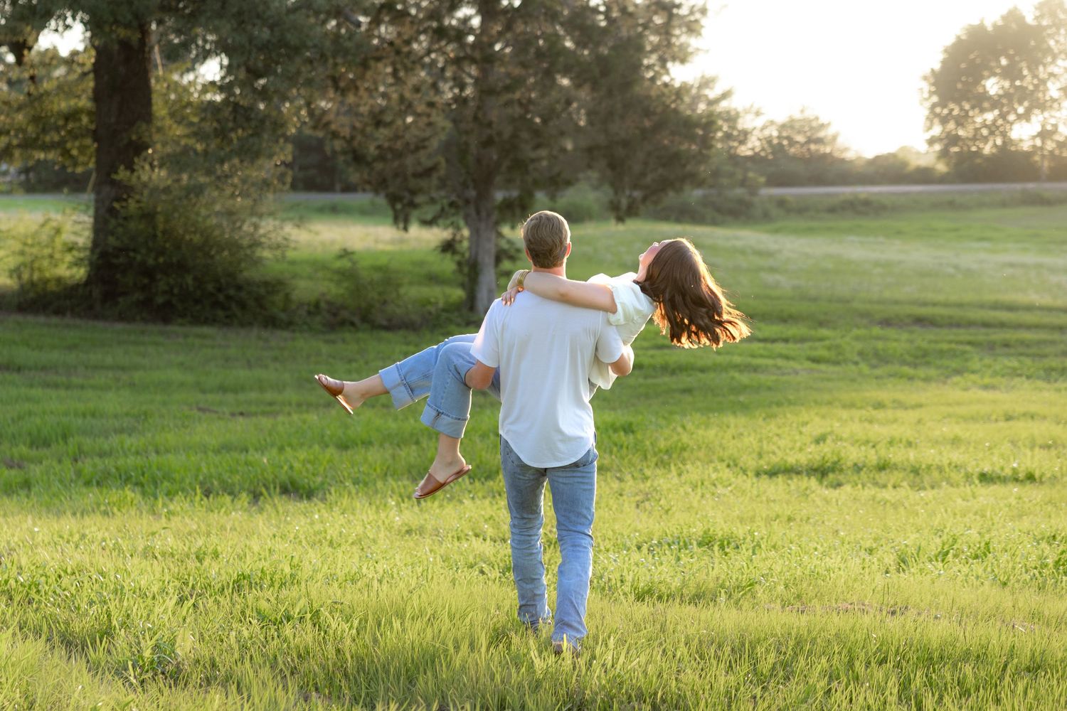 Romantic couple photos in a natural grass field setting with large trees at sunset.