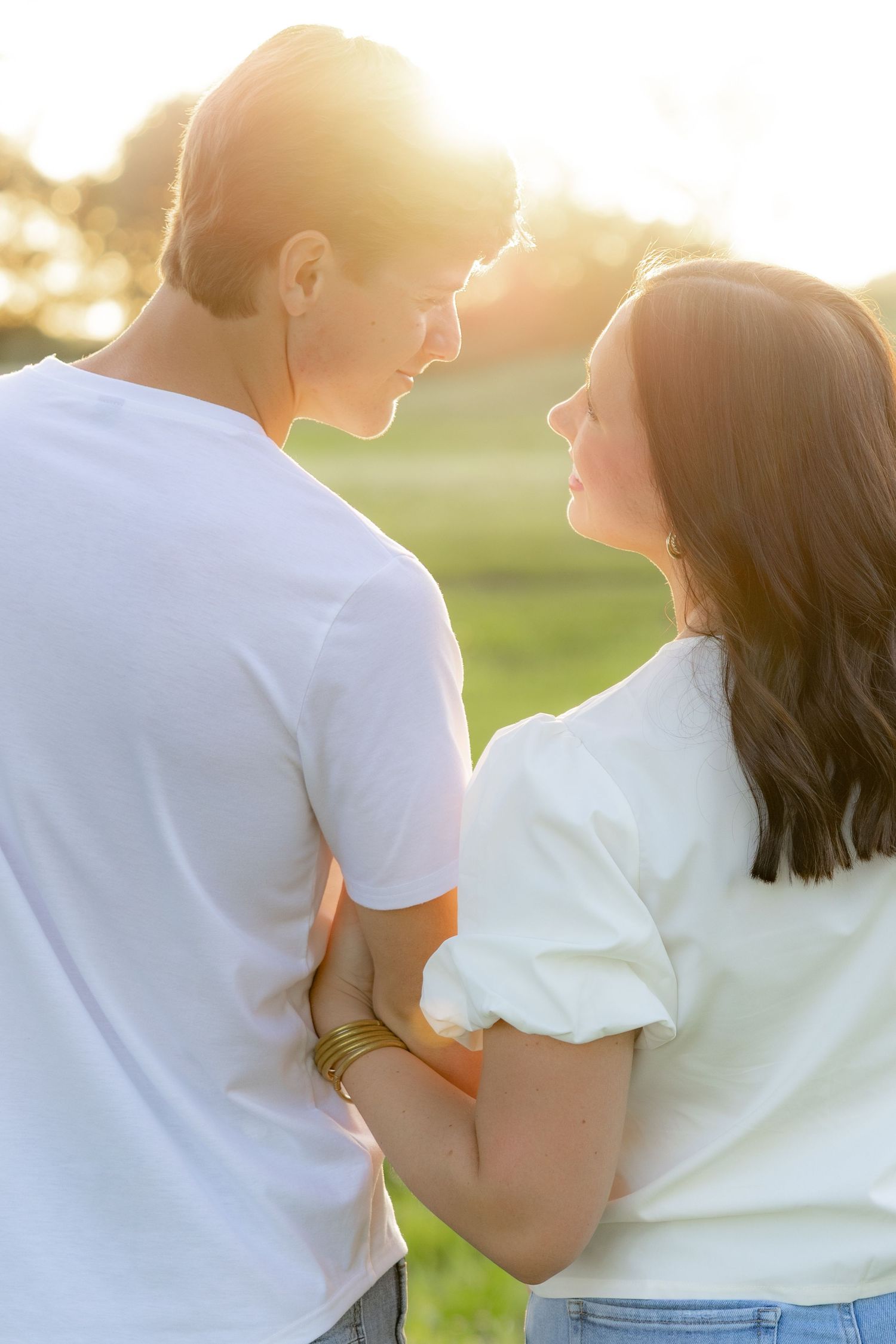 Romantic couple photos in a natural grass field setting with large trees at sunset.