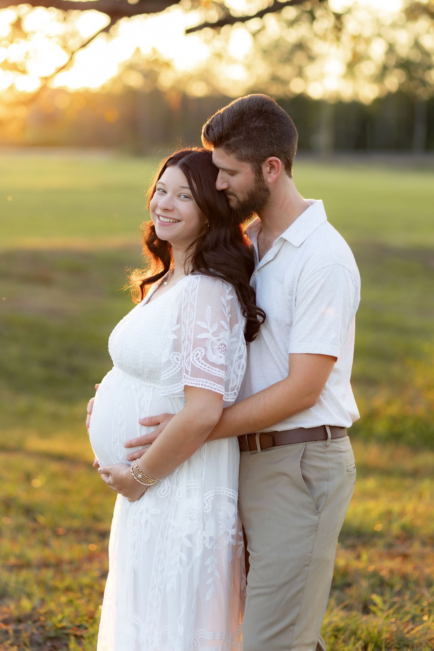 Expecting couple holding each other in a grass field at sunset in Dothan, Alabama