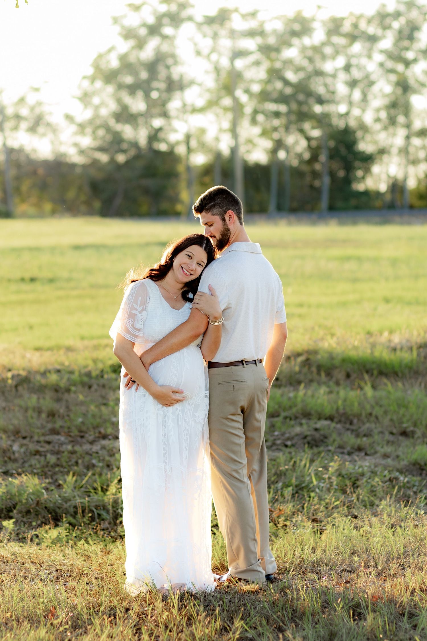 Expecting couple holding each other in a grass field at sunset in Dothan, Alabama